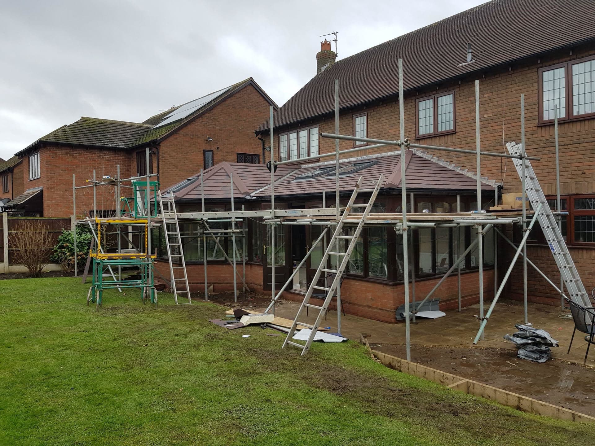 Conservatory roof replacement with brown tiled roof and scaffolding in residential garden