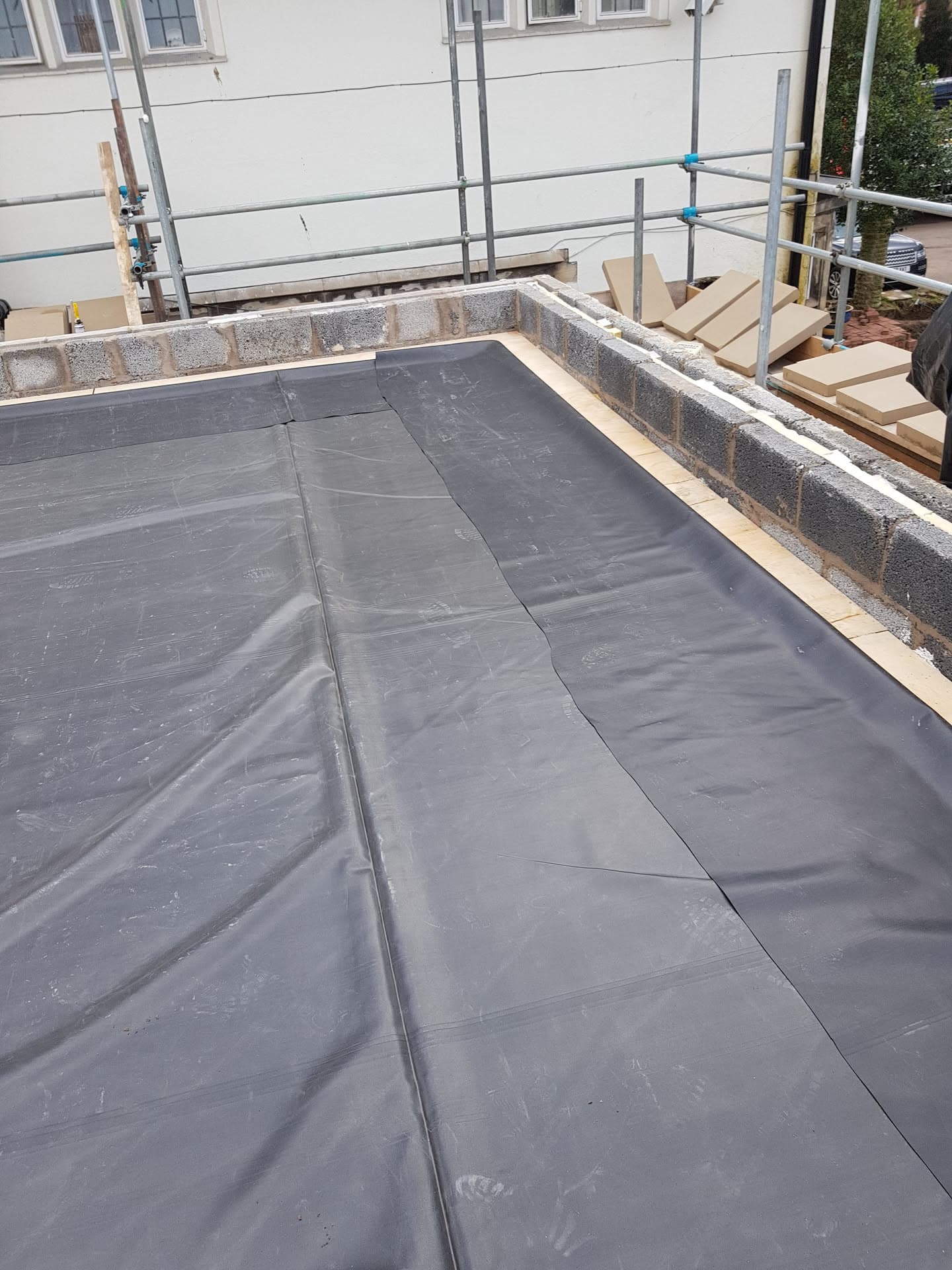 Flat roof installation with grey EPDM rubber membrane and timber edging with scaffolding