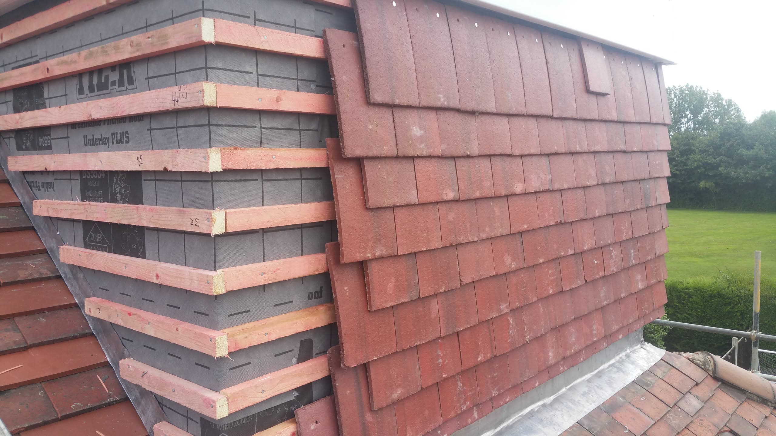 Pitched roof with red clay tiles and exposed timber battens during re-roofing work