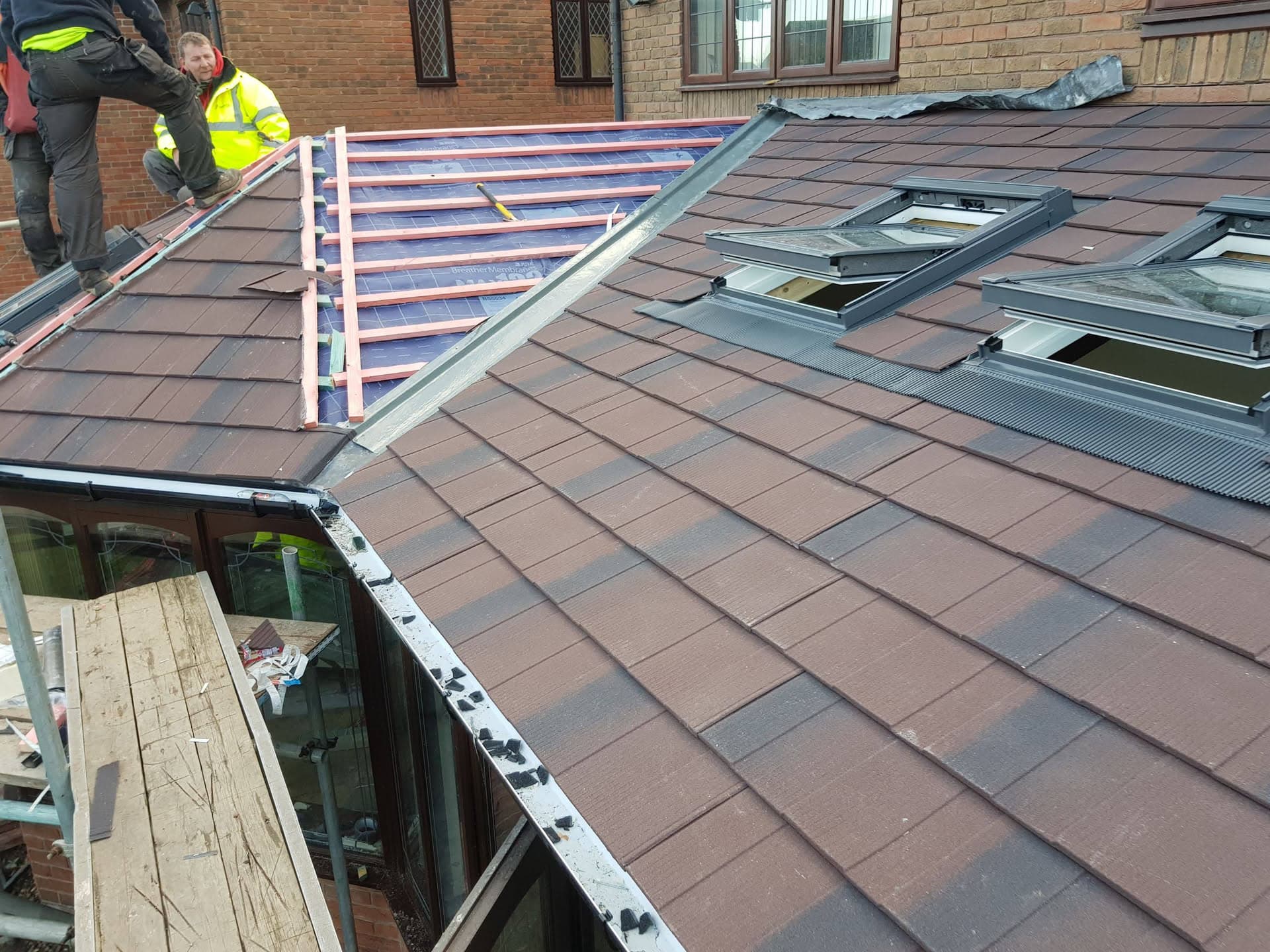 Fitter working on pitched tiled roof with conservatory extension and roof windows being installed