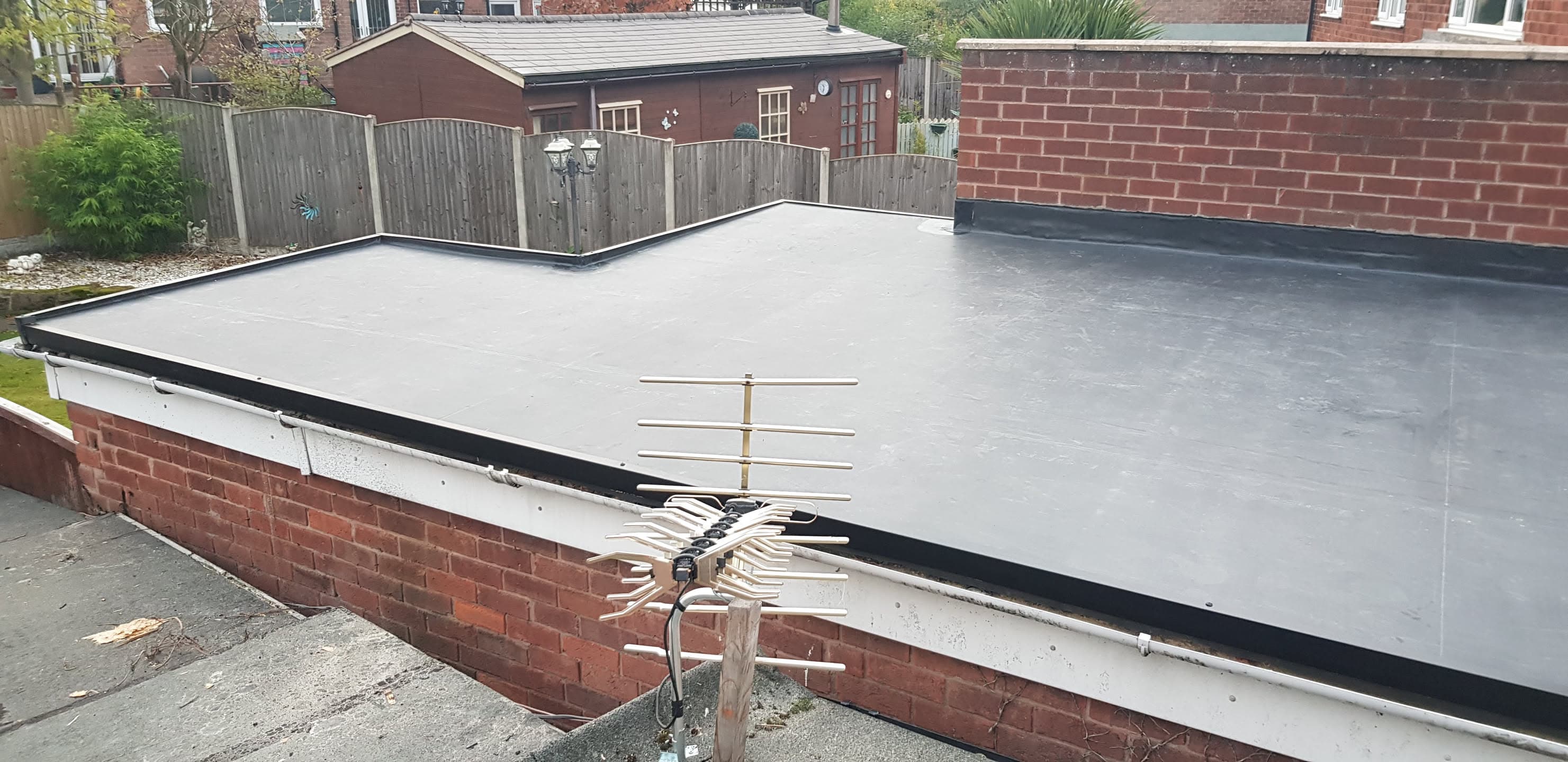 Grey flat roof installation on brick extension with black trim edging