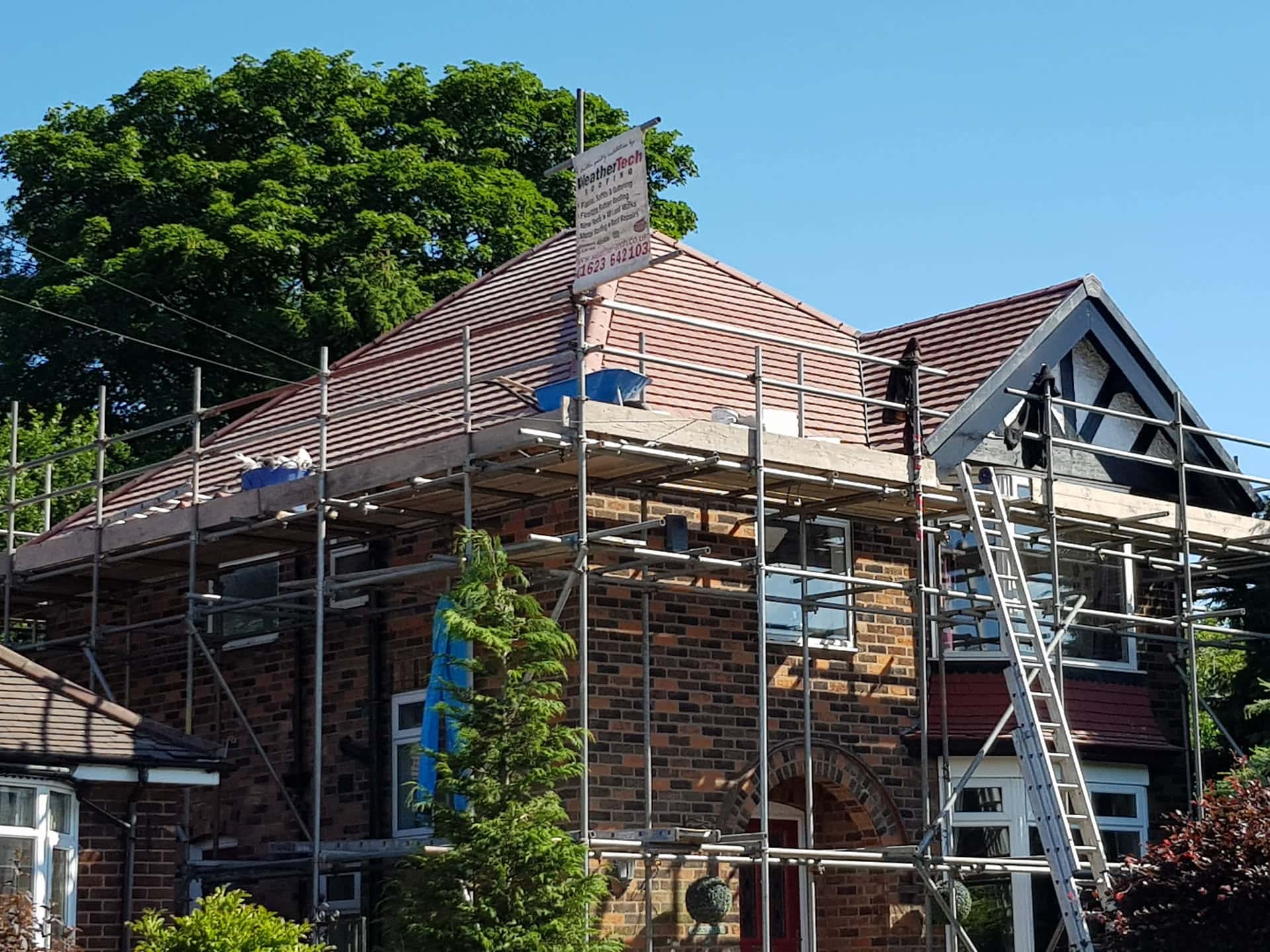 Pitched roof re-tiling in progress with clay tiles and scaffolding on brick house