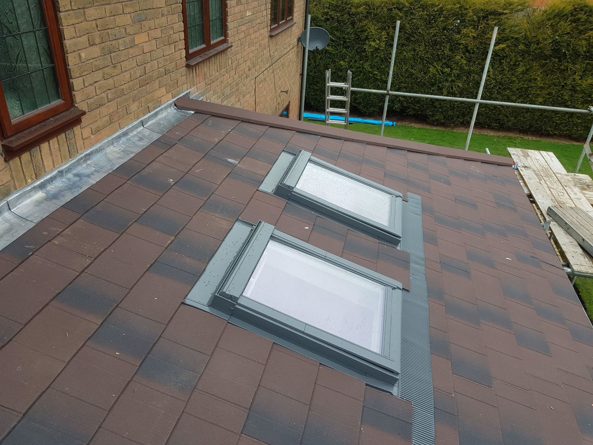 Flat roof with brown concrete tiles and two grey-framed skylights with lead flashing