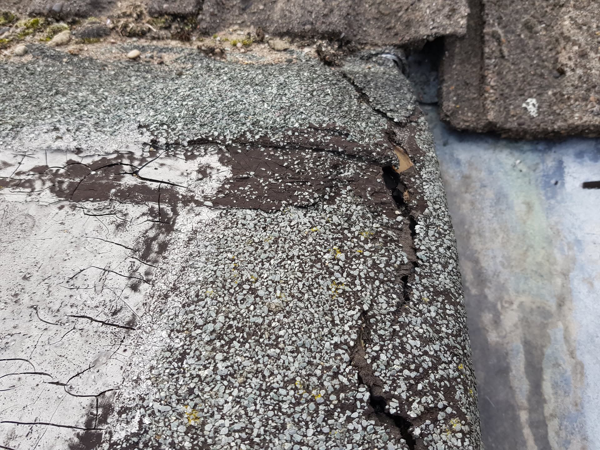 Deteriorated flat roof surface showing cracking, blistering and exposed felt layers
