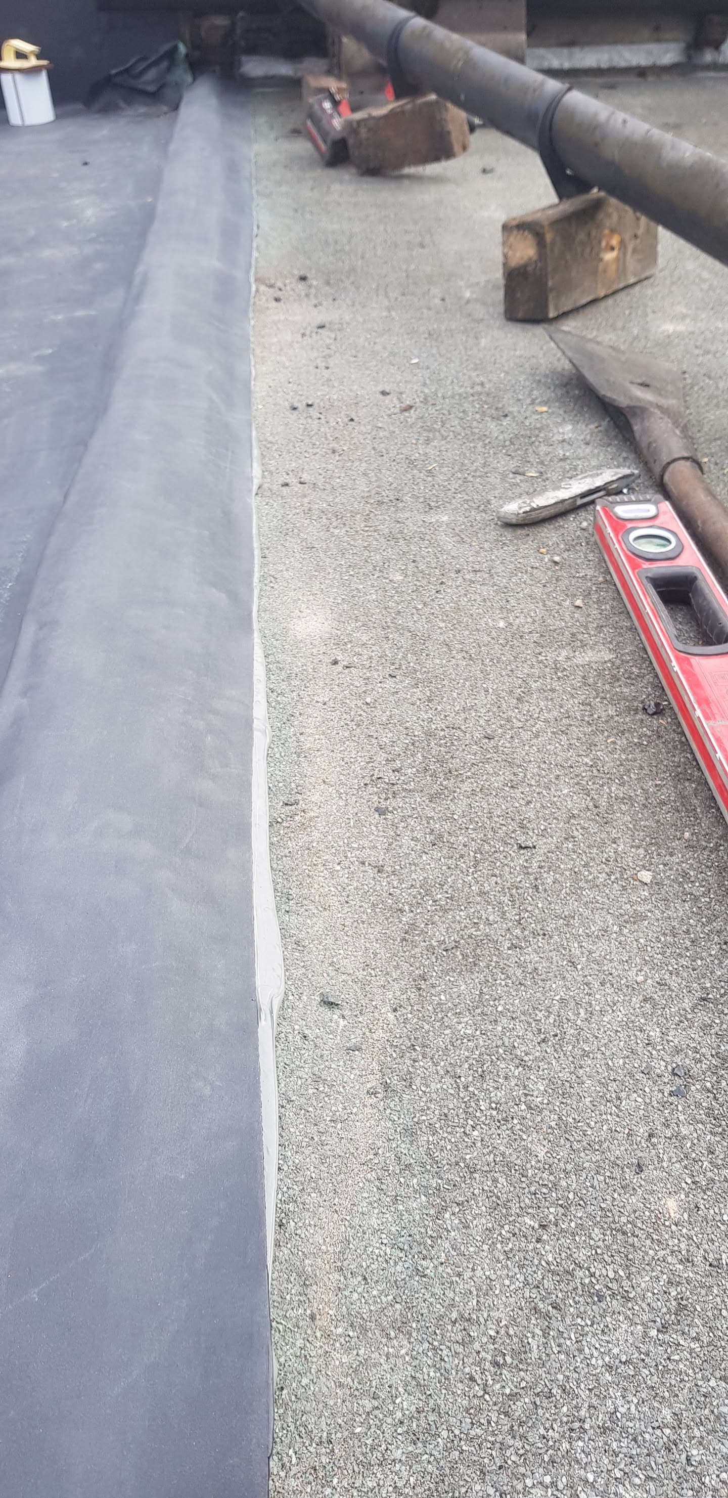 Flat roof installation in progress with grey felt membrane and tools on surface