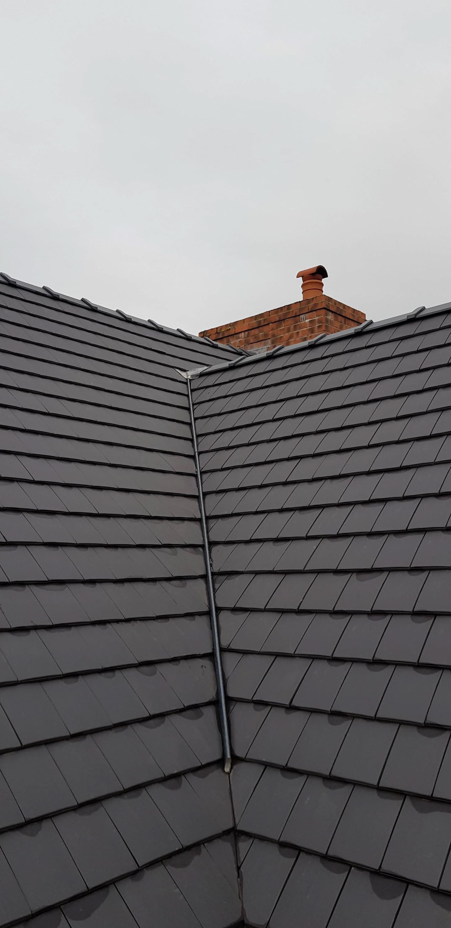 Grey slate pitched roof with valley and red brick chimney stack