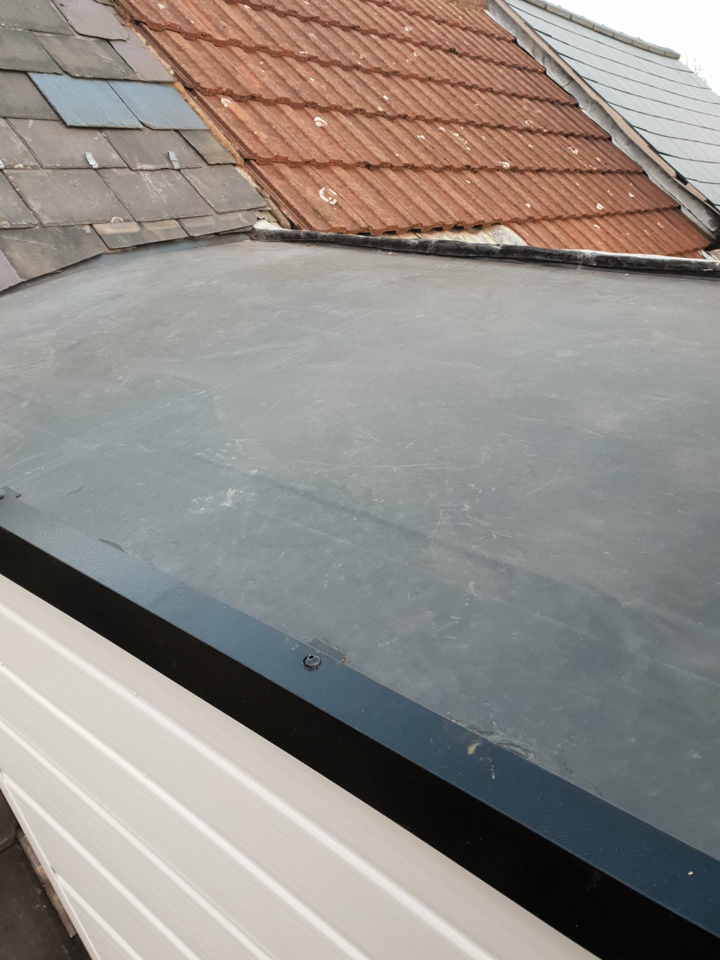 Flat roof with grey EPDM membrane meeting terracotta tiled pitched roof and grey slate roof