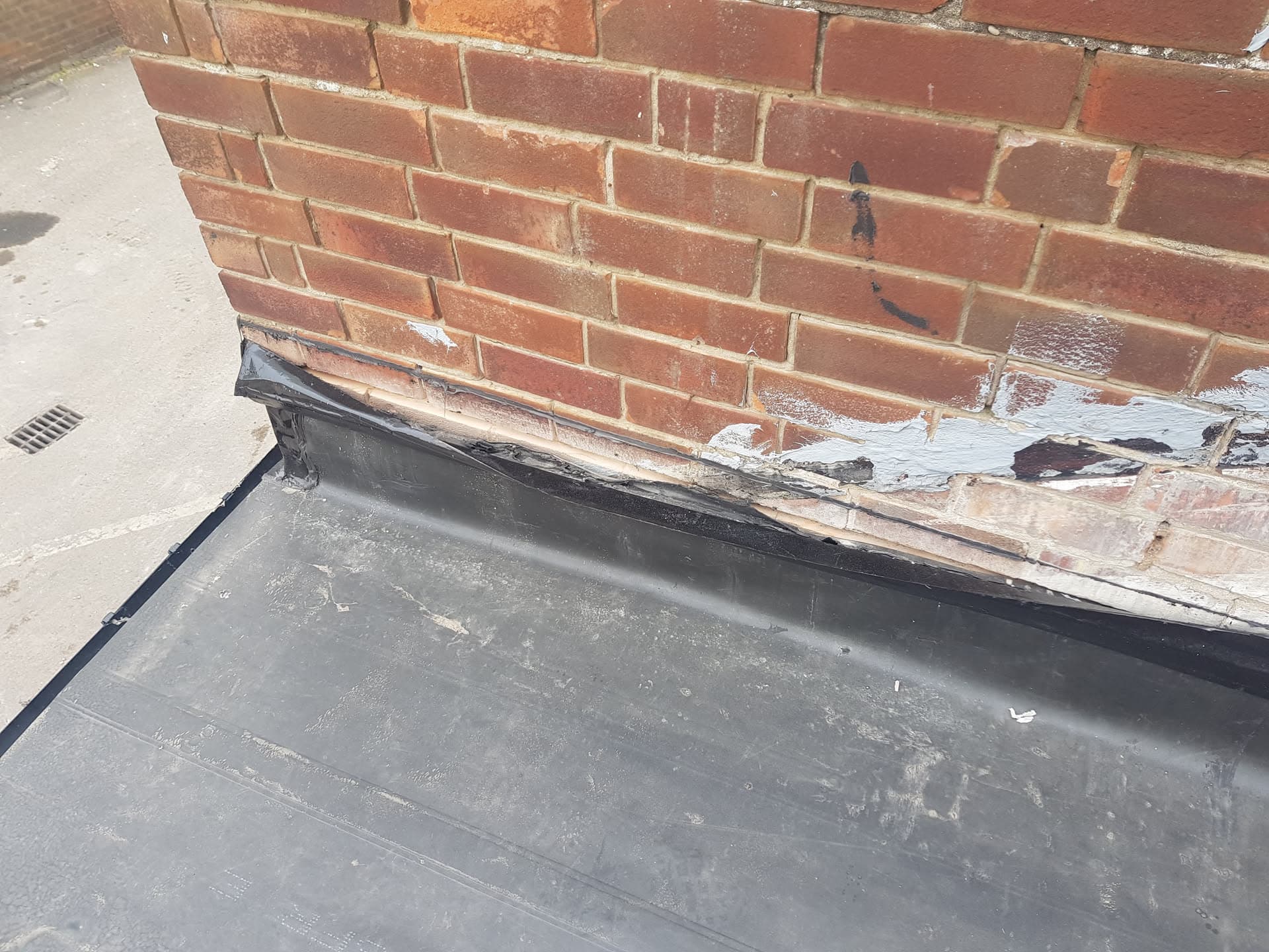 Lead flashing detail at brick wall junction on flat roof showing weathered timber fascia