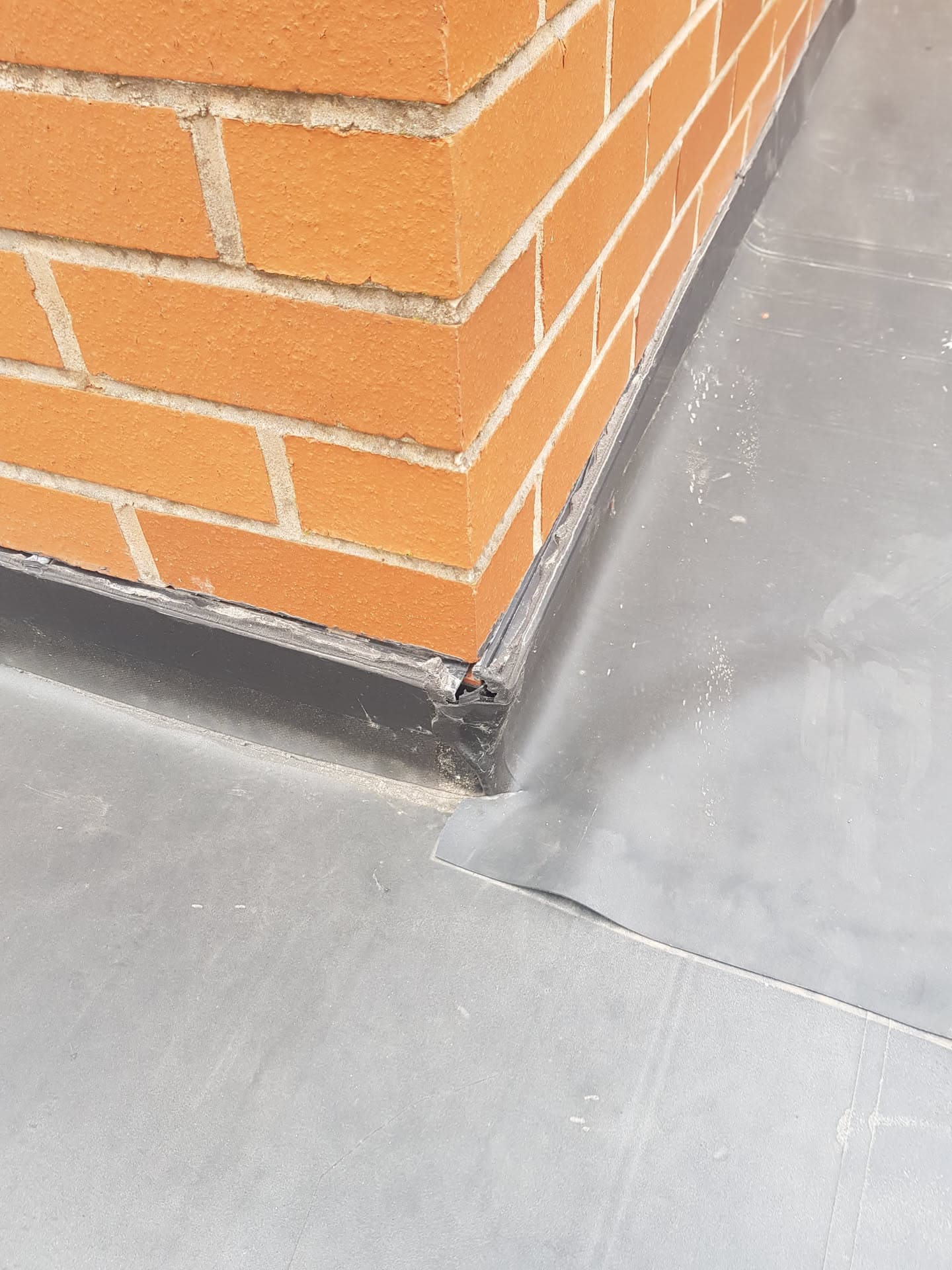 Lead flashing installed around brick chimney stack on grey flat roof
