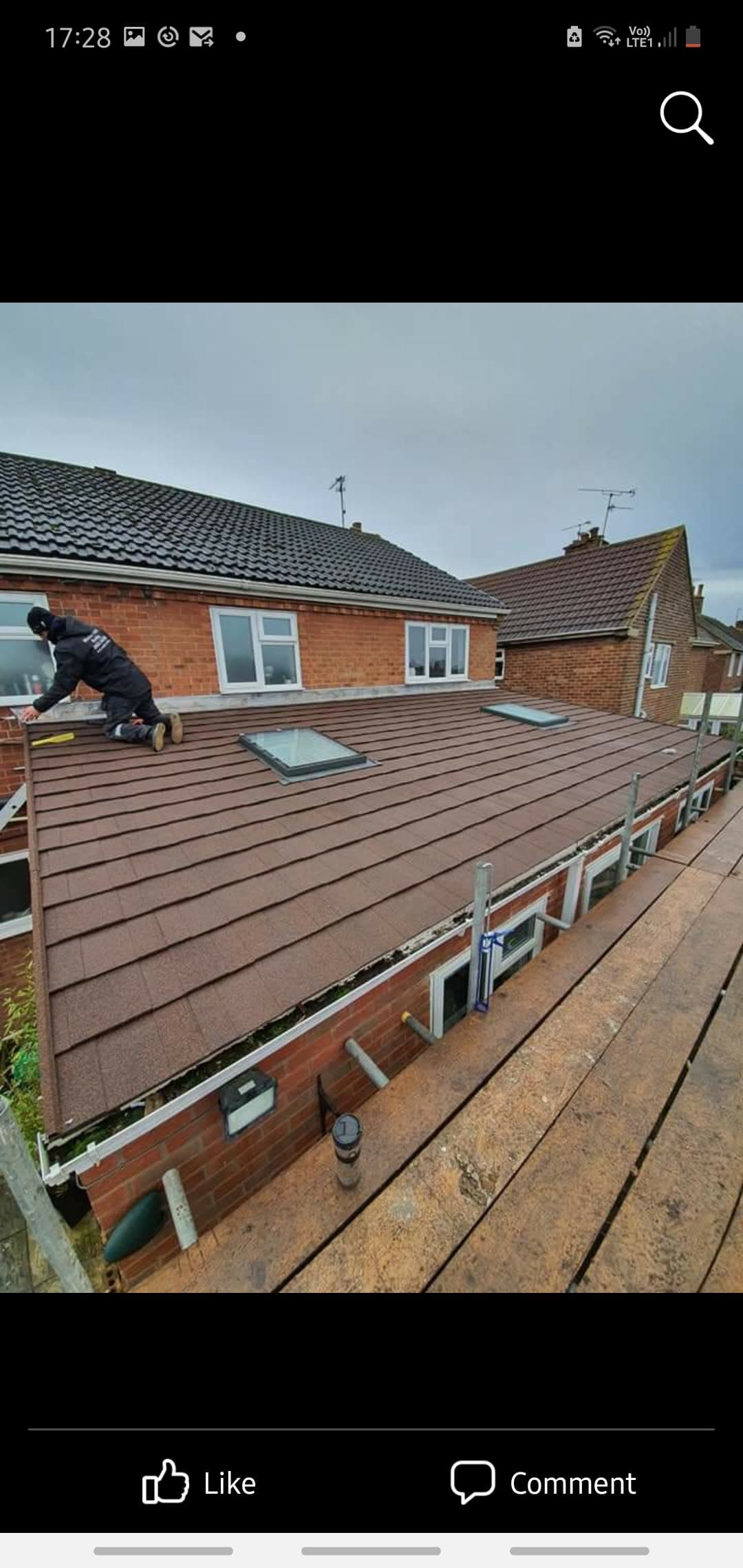 Fitter installing brown composite decking on flat roof extension with skylight