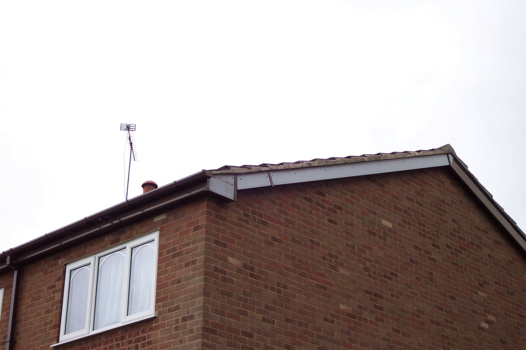 Pitched roof with brown concrete tiles, white fascias and soffits on brick gable end