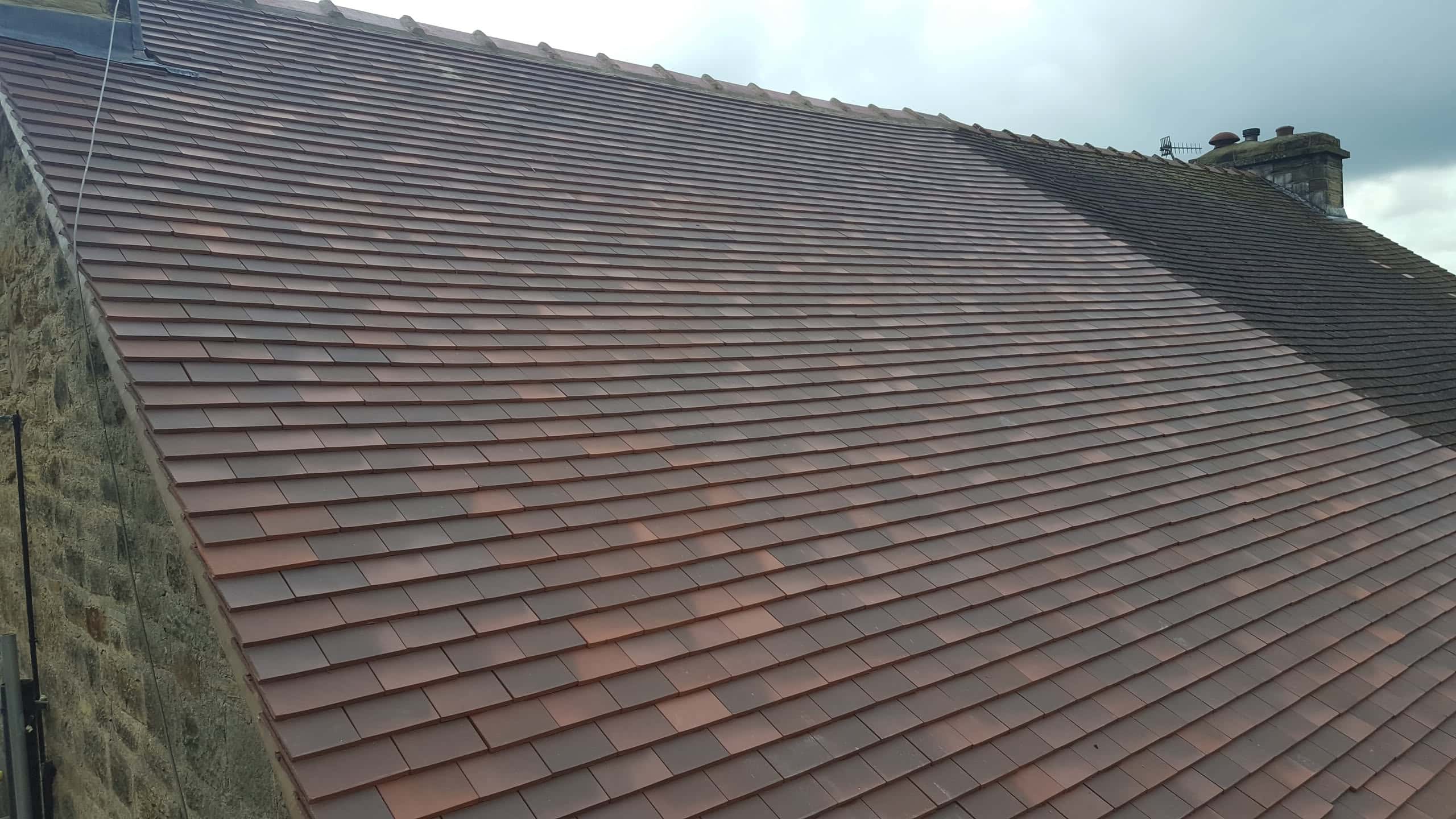Newly completed pitched roof with terracotta clay tiles and ridge line