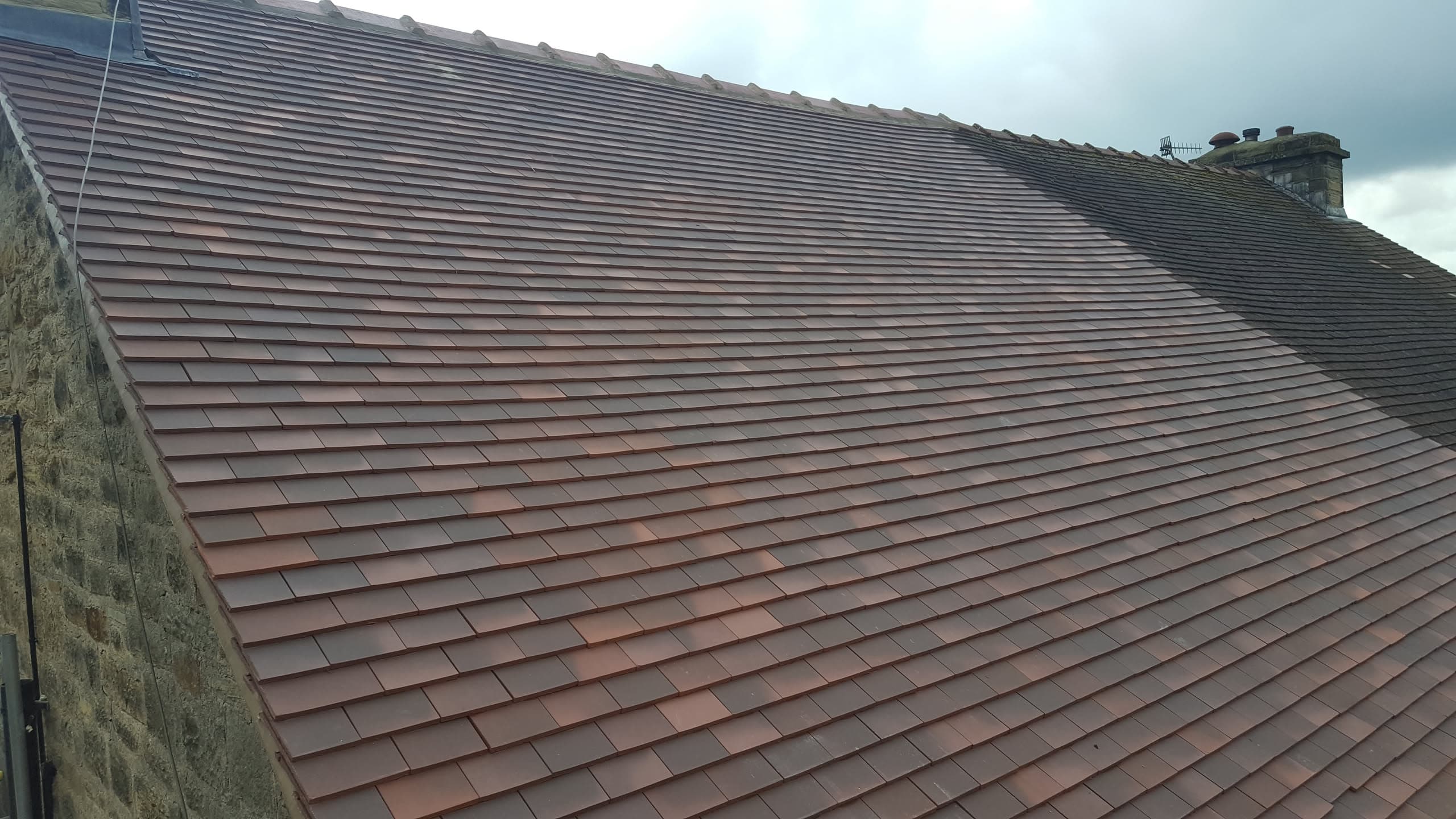 Newly completed pitched roof with terracotta clay tiles and ridge line