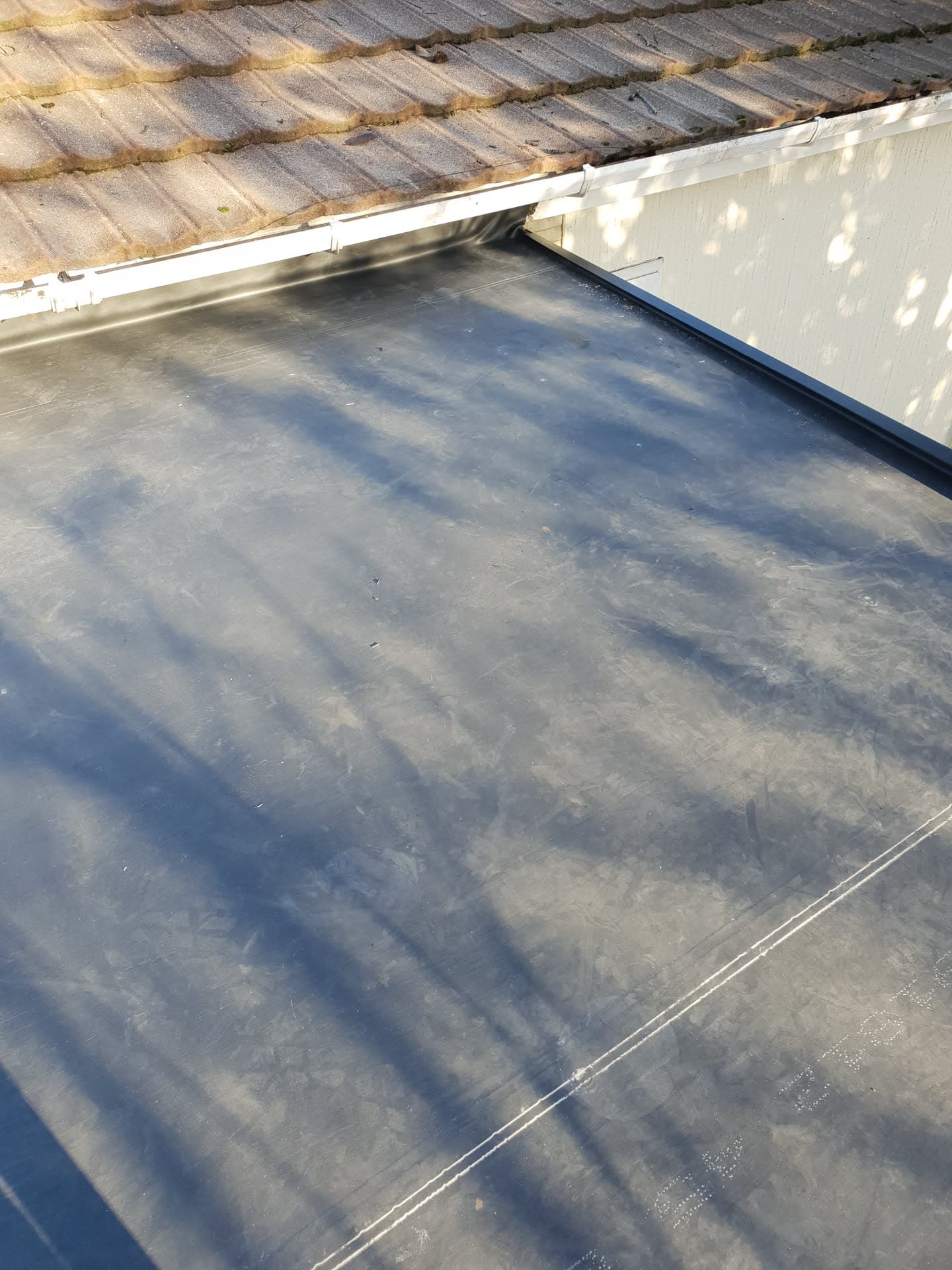 Flat roof with EPDM rubber membrane meeting pitched concrete tiled roof with white fascia and guttering