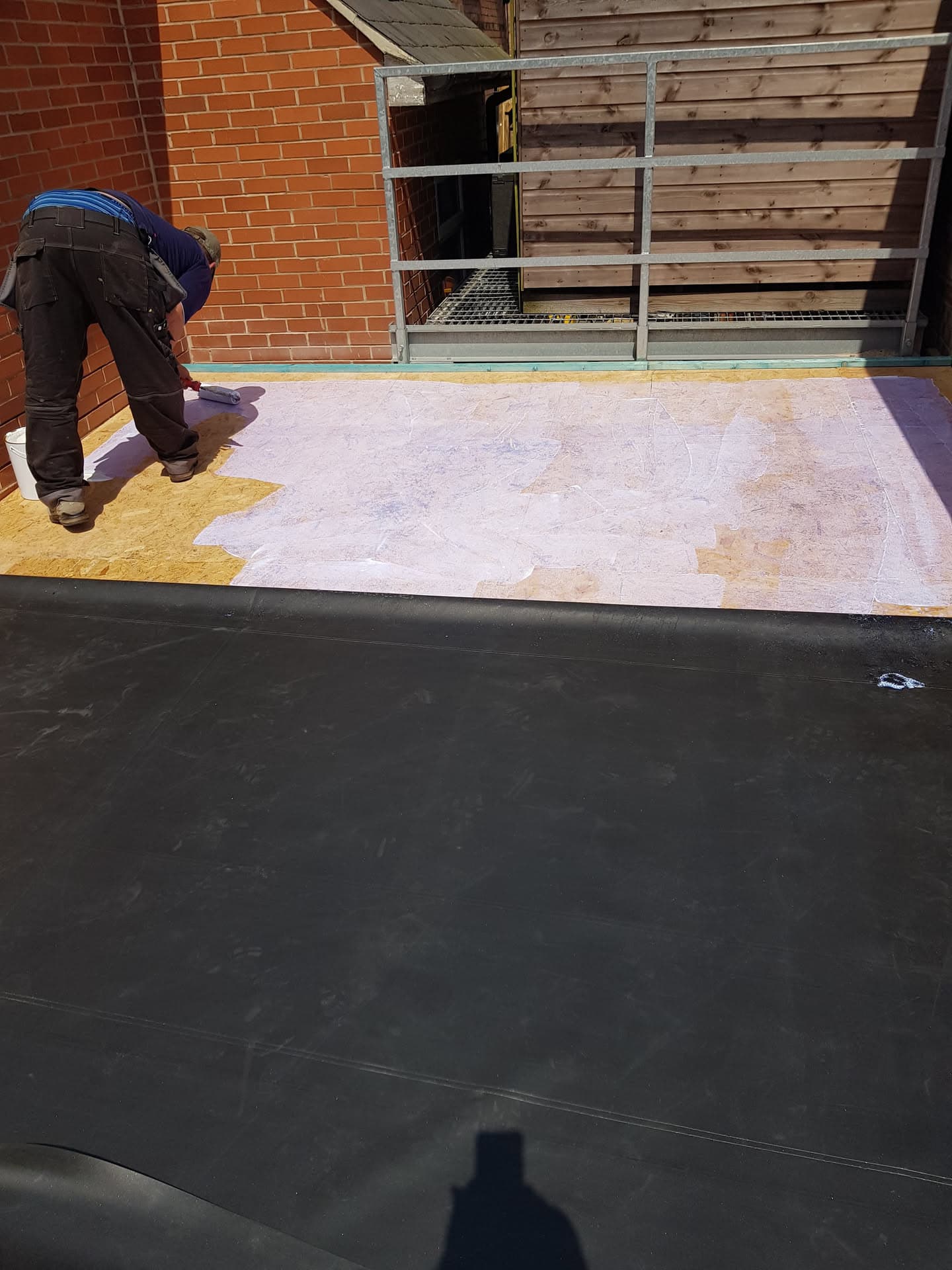 Fitter applying GRP fibreglass coating to flat roof with scaffolding access