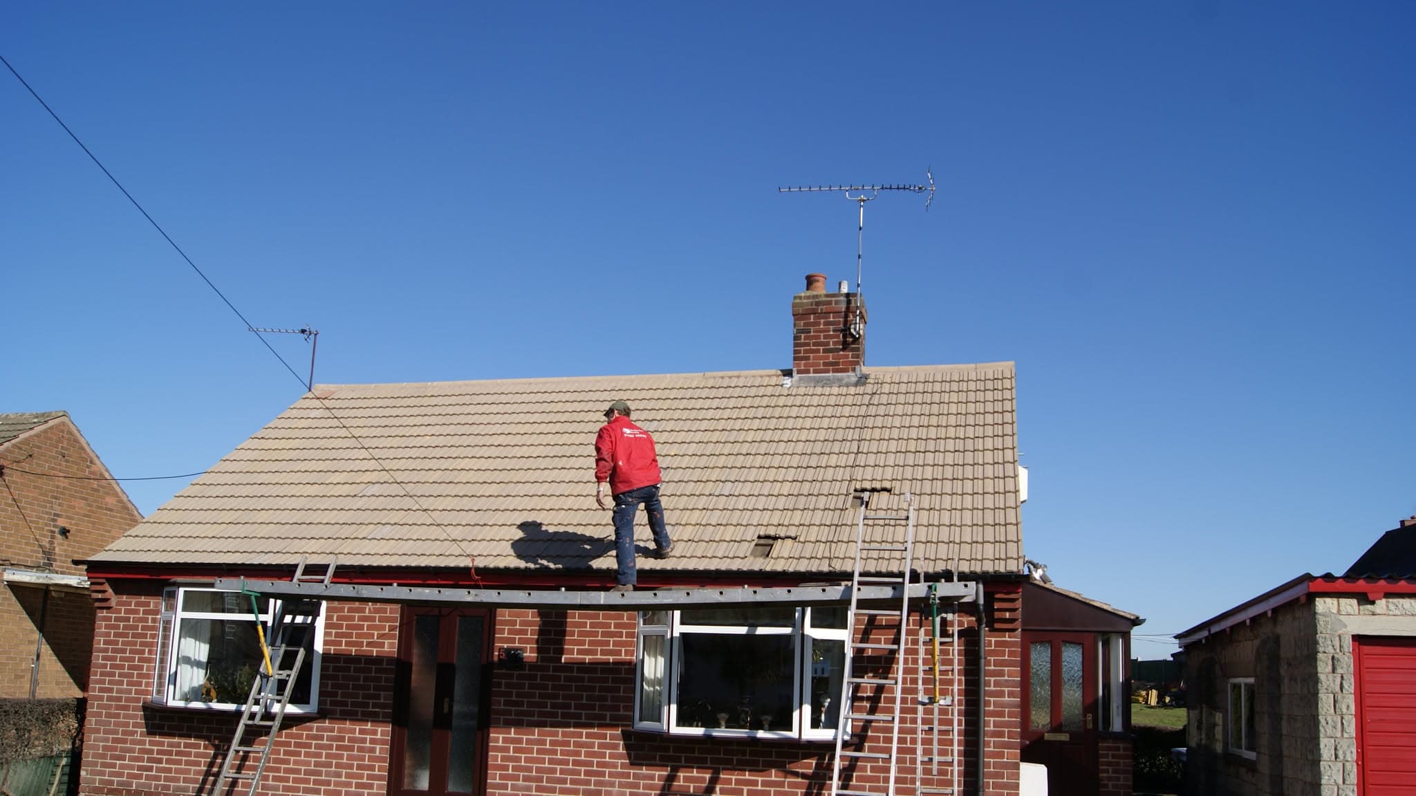 Fitter in red jacket working on pitched concrete tiled roof with brick chimney