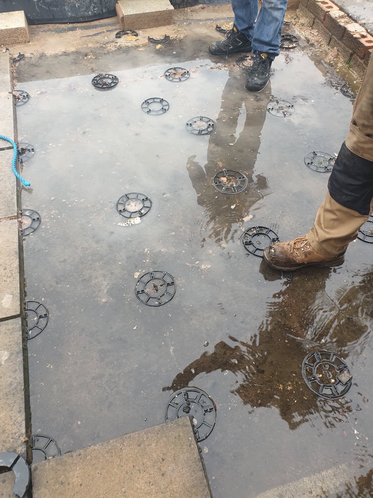Fitter standing on grey flat roof with plastic support pads during installation