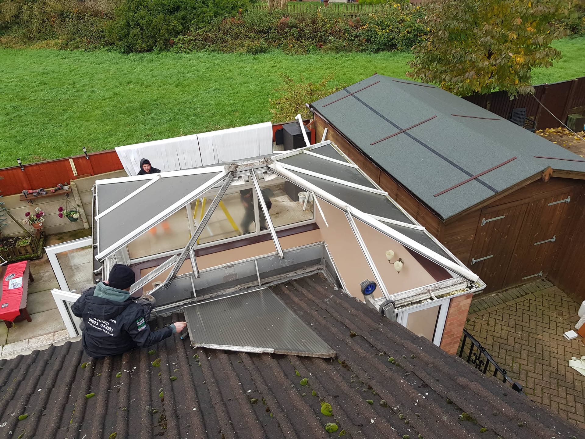 Fitter installing conservatory roof with grey panels and white aluminium frame