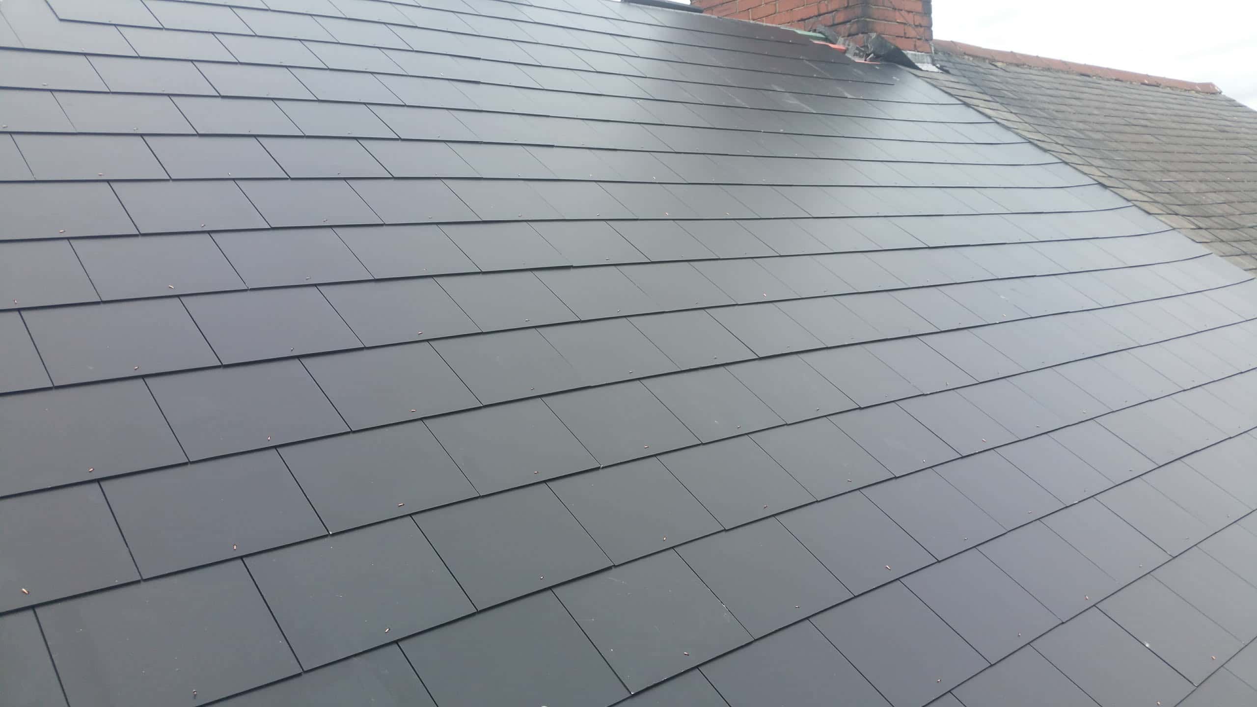 Newly installed grey slate pitched roof with brick chimney stack