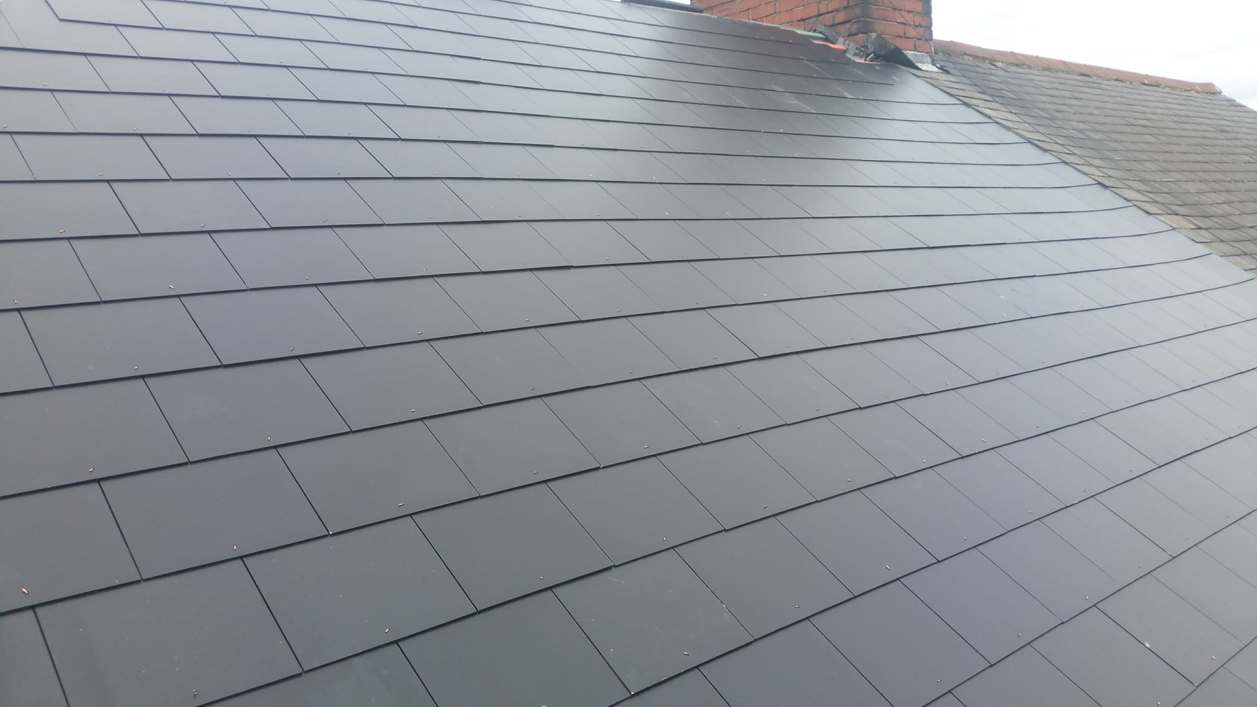 Newly installed grey slate pitched roof with brick chimney stack