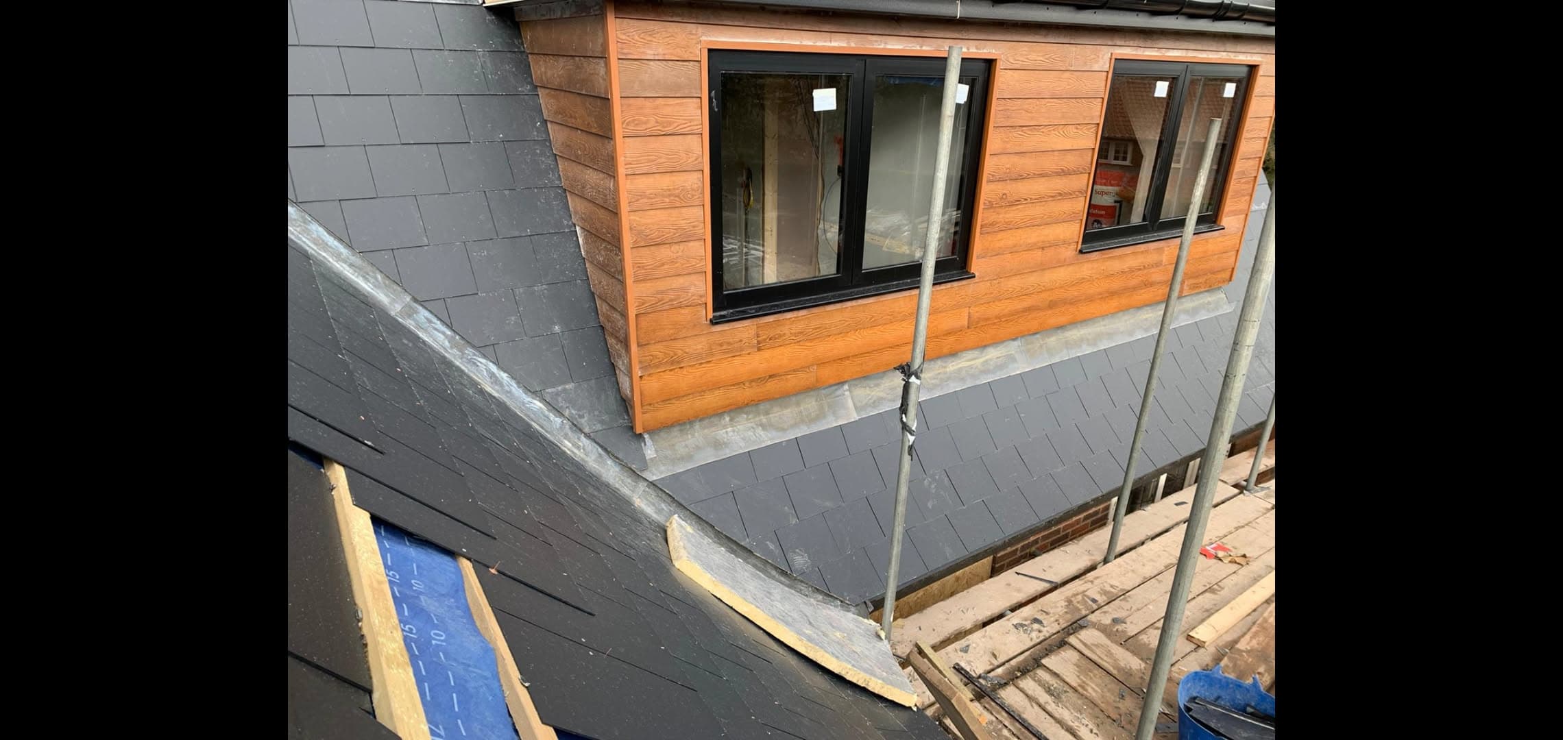 Grey slate pitched roof with dormer featuring timber cladding and black windows