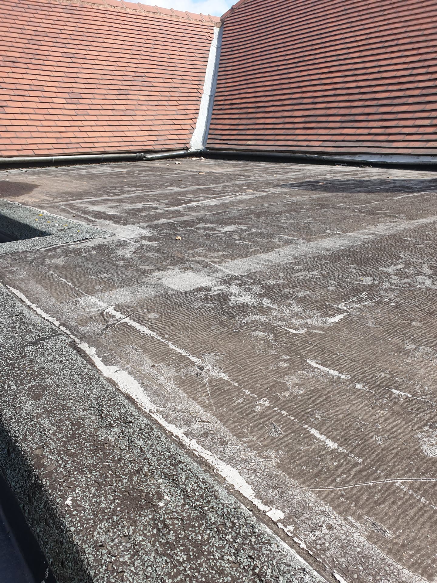 Flat roof with felt surface meeting two pitched tiled roofs at valley junction