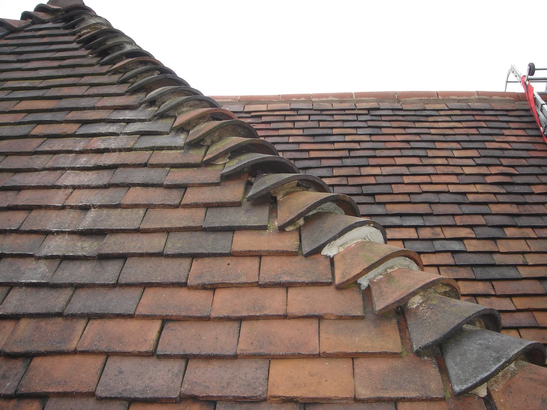 Pitched roof with terracotta clay tiles and curved ridge tiles meeting at the apex