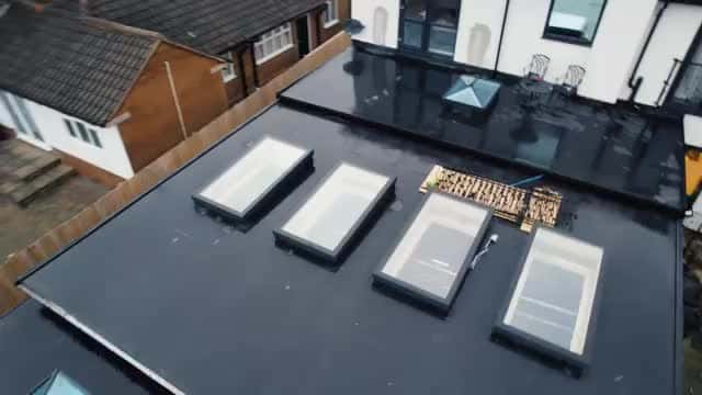 Dark grey flat roof with four rectangular rooflights on modern extension