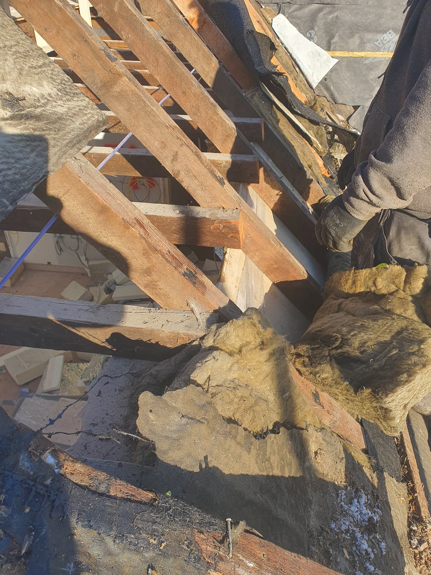 Pitched roof repair in progress showing exposed timber rafters and old insulation being removed