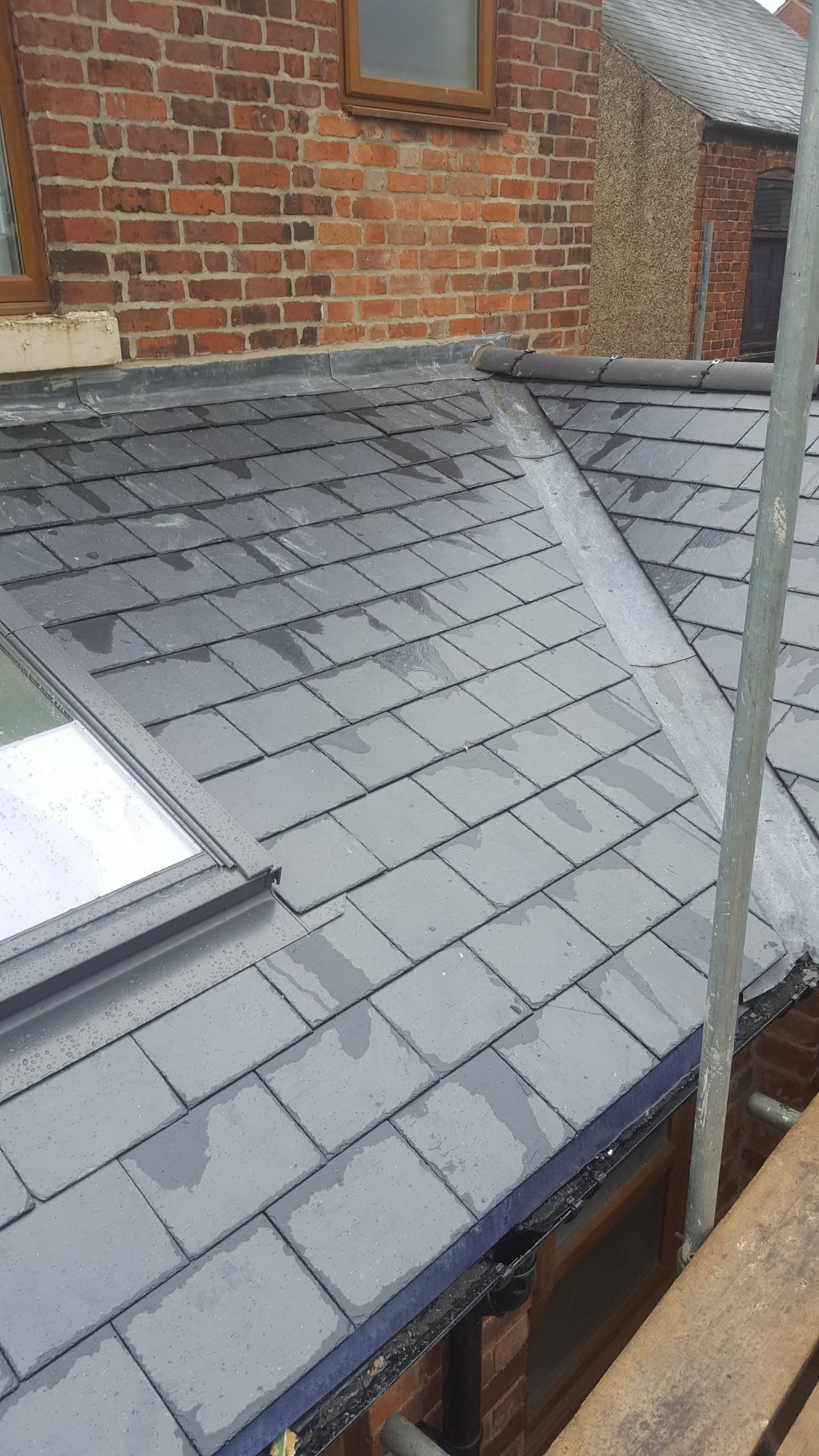 Grey slate pitched roof with lead valley and ridge against red brick wall