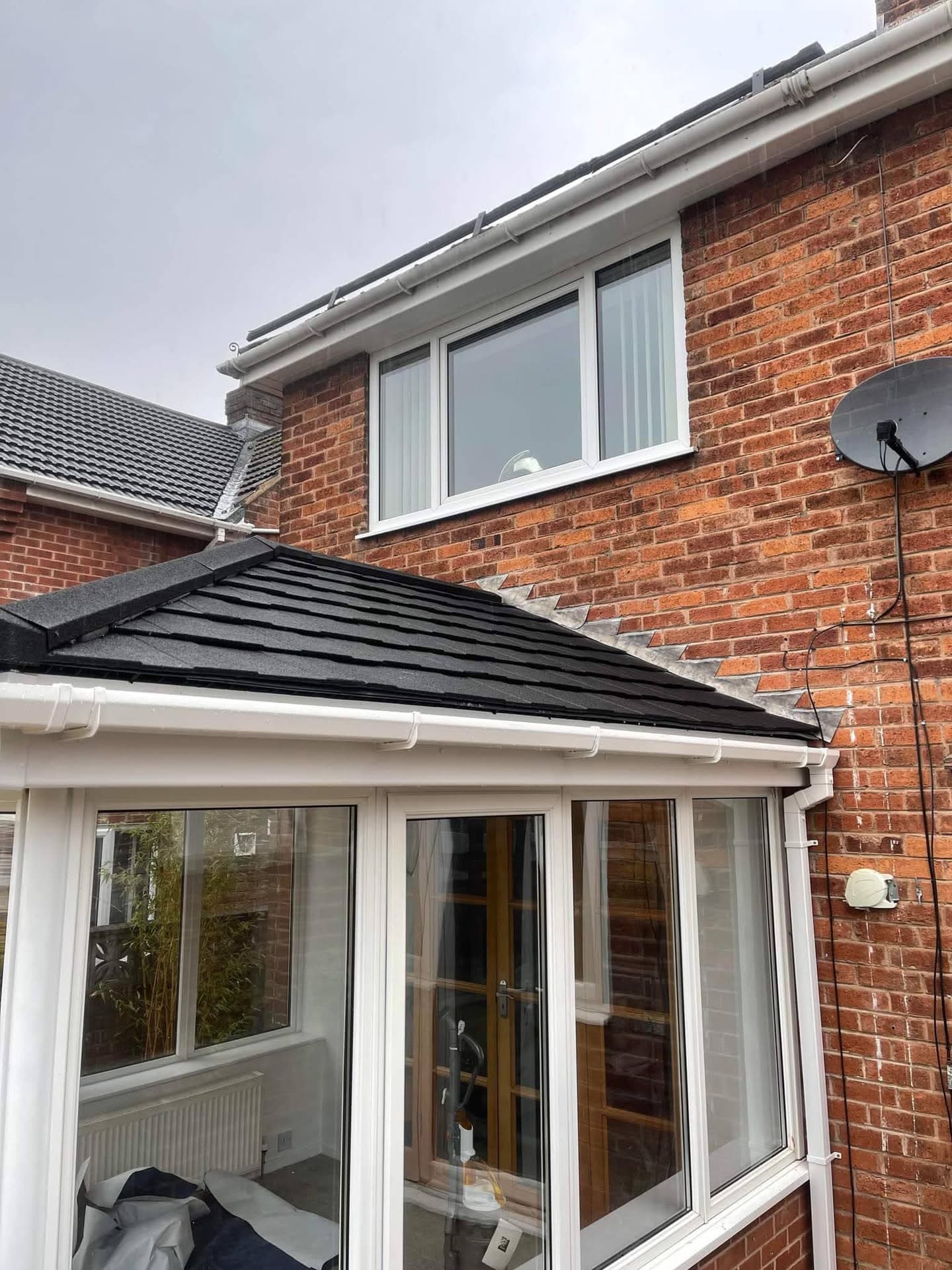 Conservatory with dark tiled roof and white fascias and guttering on brick house