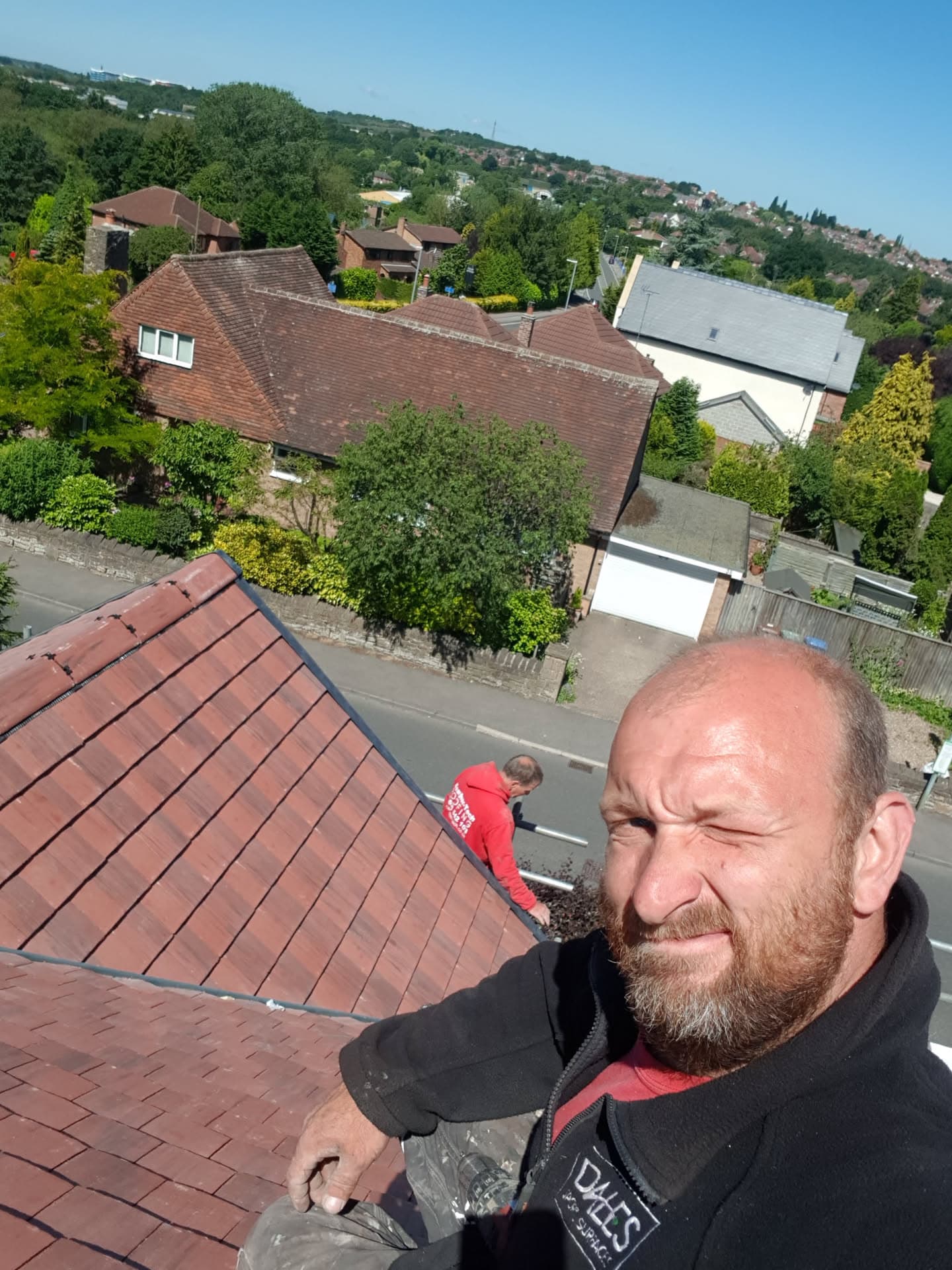 Two fitters working on a pitched roof with red concrete tiles