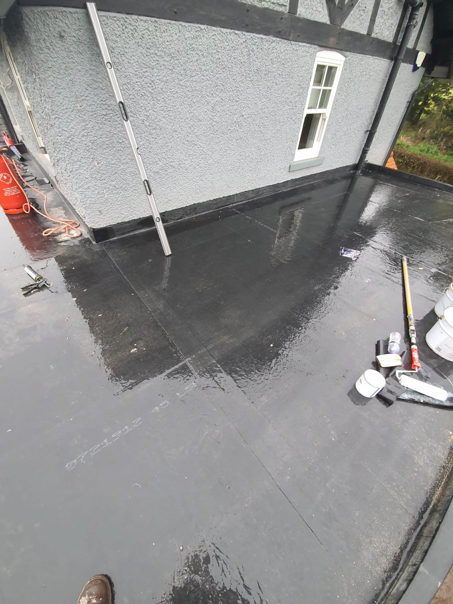 Flat roof with dark grey felt covering and ladder against rendered wall