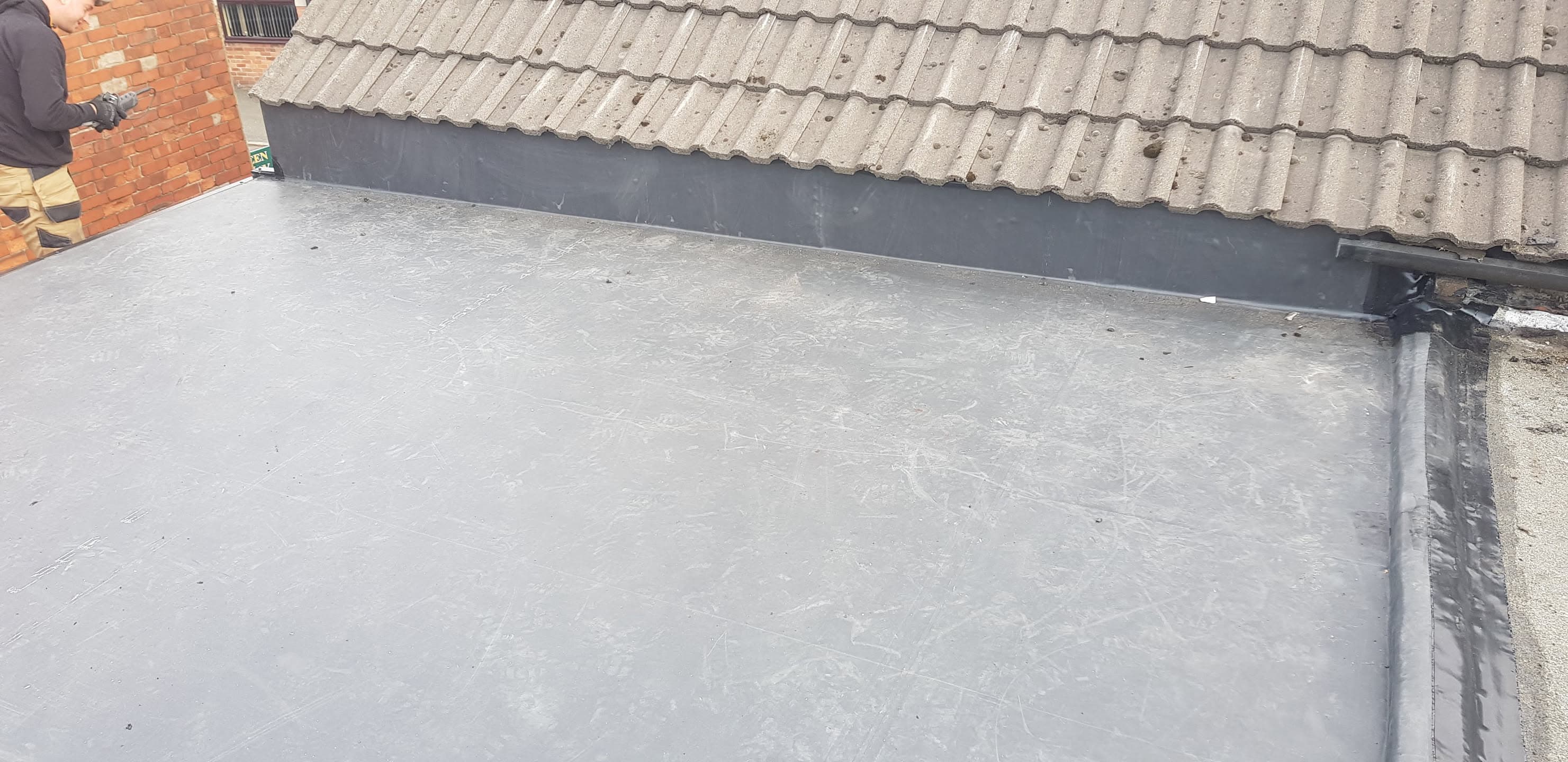 Grey flat roof with lead flashing against concrete tiled pitched roof and brick chimney
