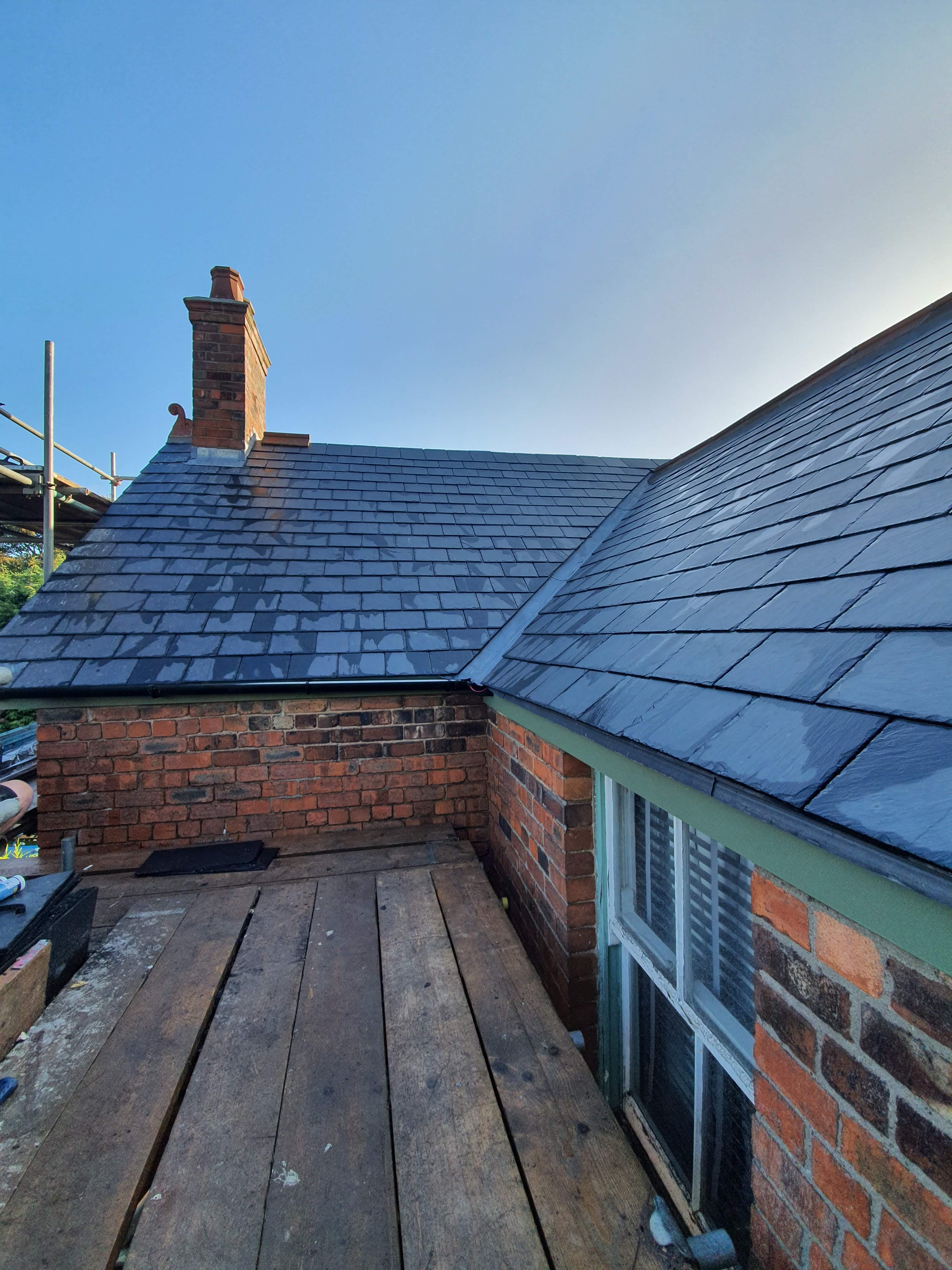 Pitched slate roof with brick chimney stack and scaffolding visible