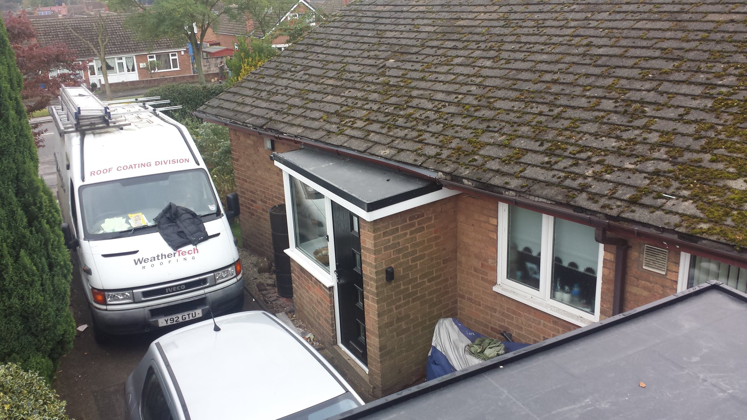 WeatherTech van parked beside bungalow with moss-covered tiled roof and flat roof porch extension