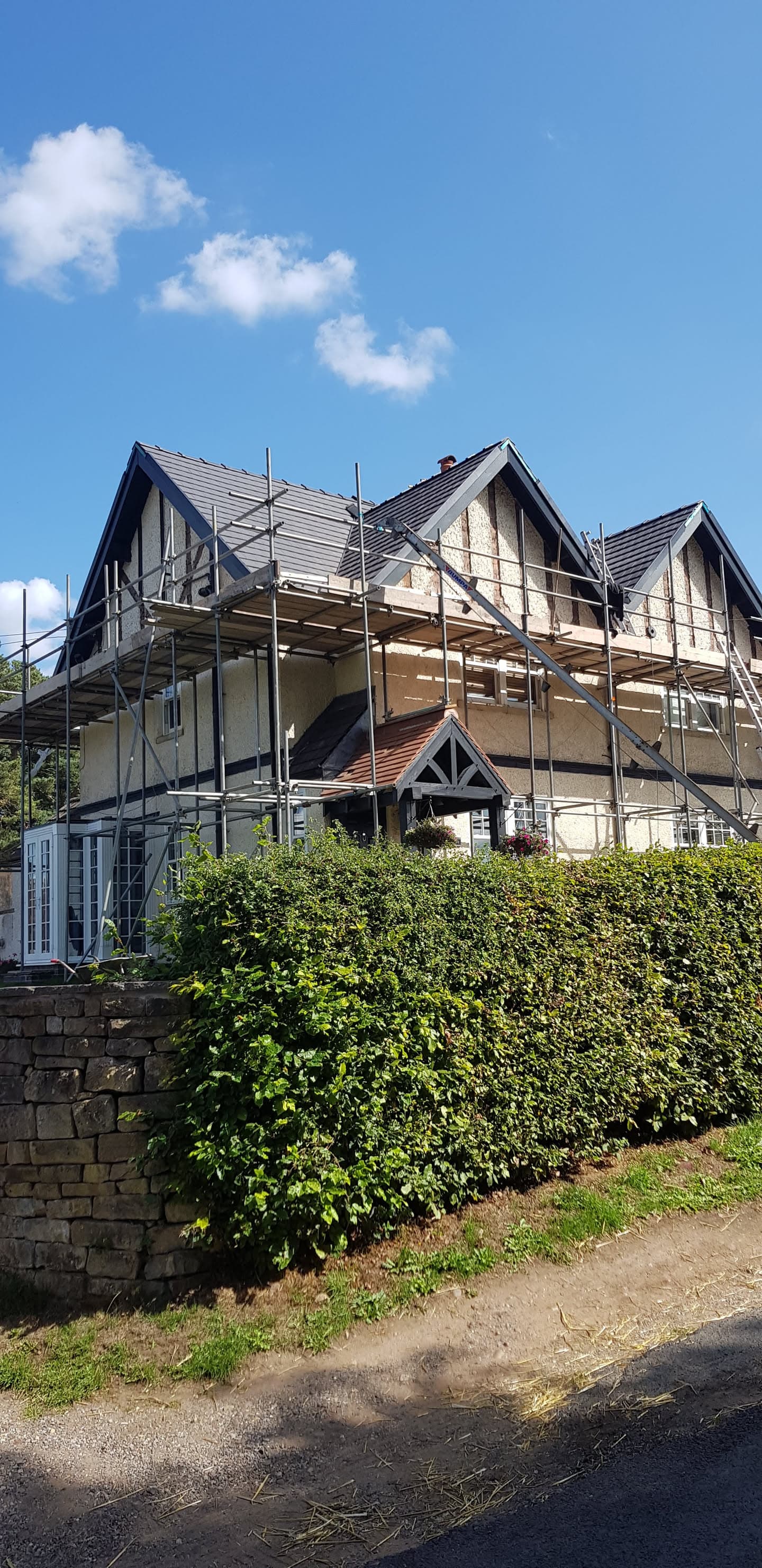 Large detached house with pitched tiled roof and scaffolding erected for roofing work