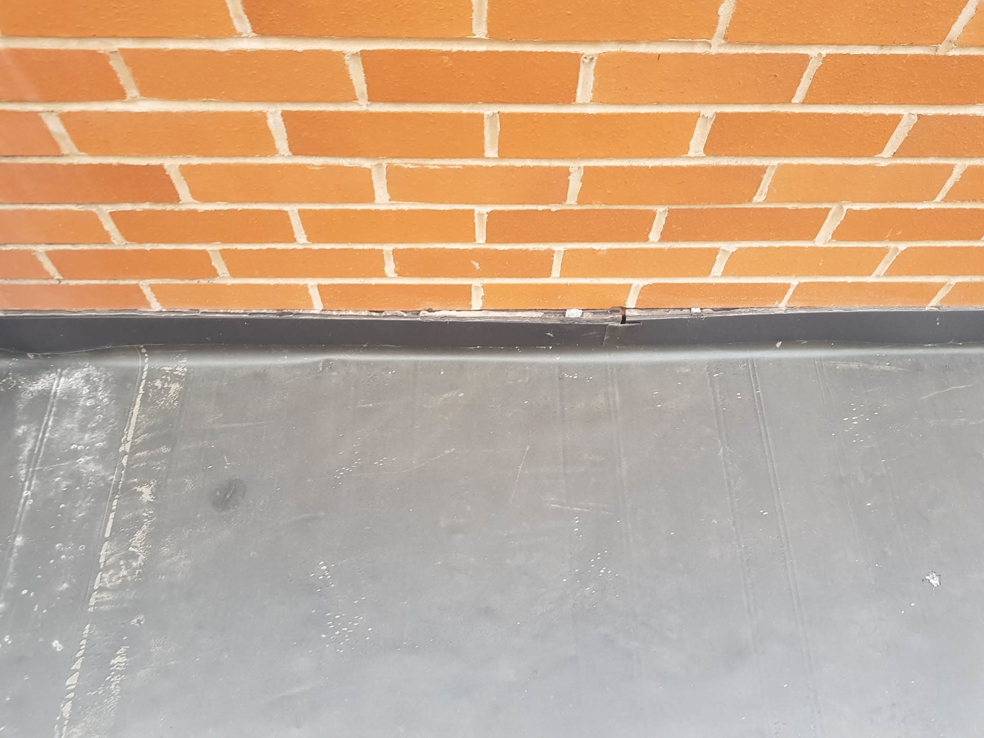 Grey flat roof with lead flashing against orange brick wall