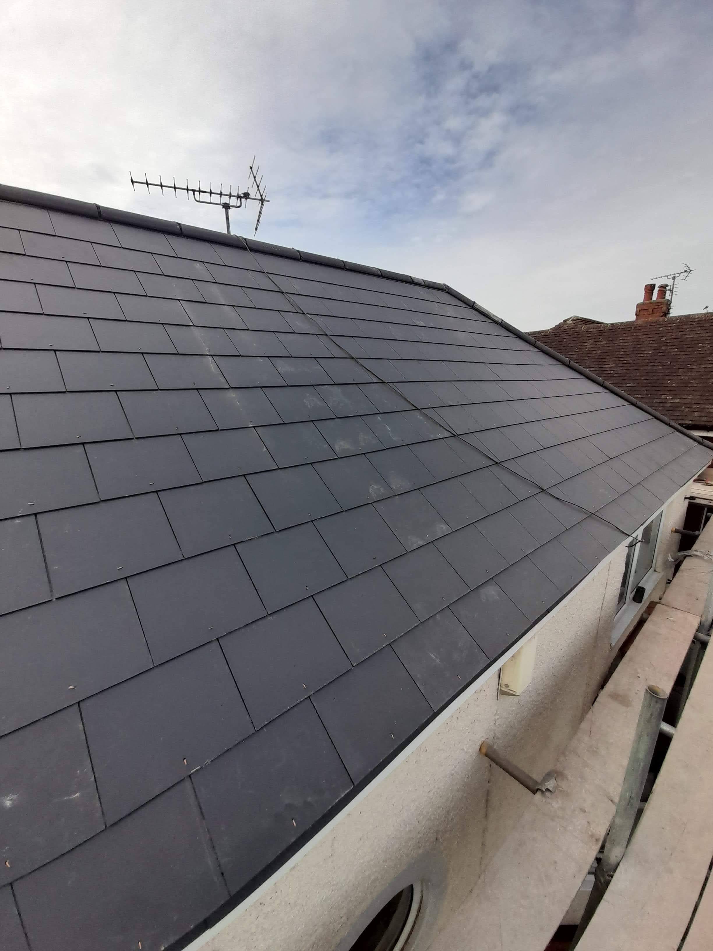 Newly completed pitched roof with dark grey slate tiles and TV aerial
