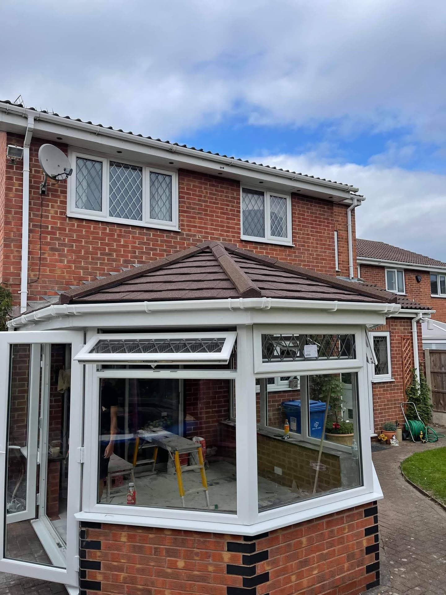 Brown tiled conservatory roof on brick house with white uPVC fascias and guttering