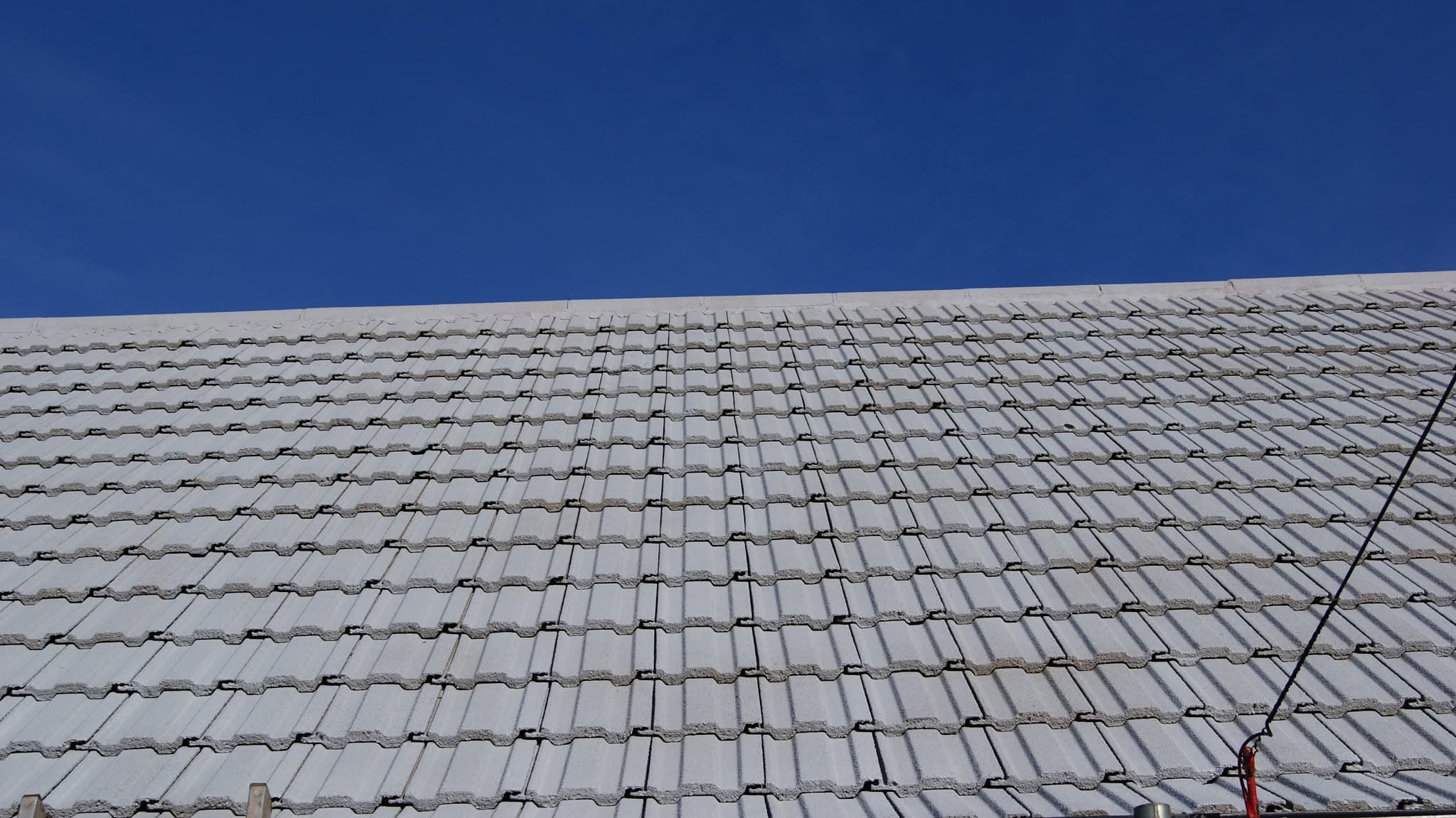 Pitched roof with grey concrete tiles against clear blue sky