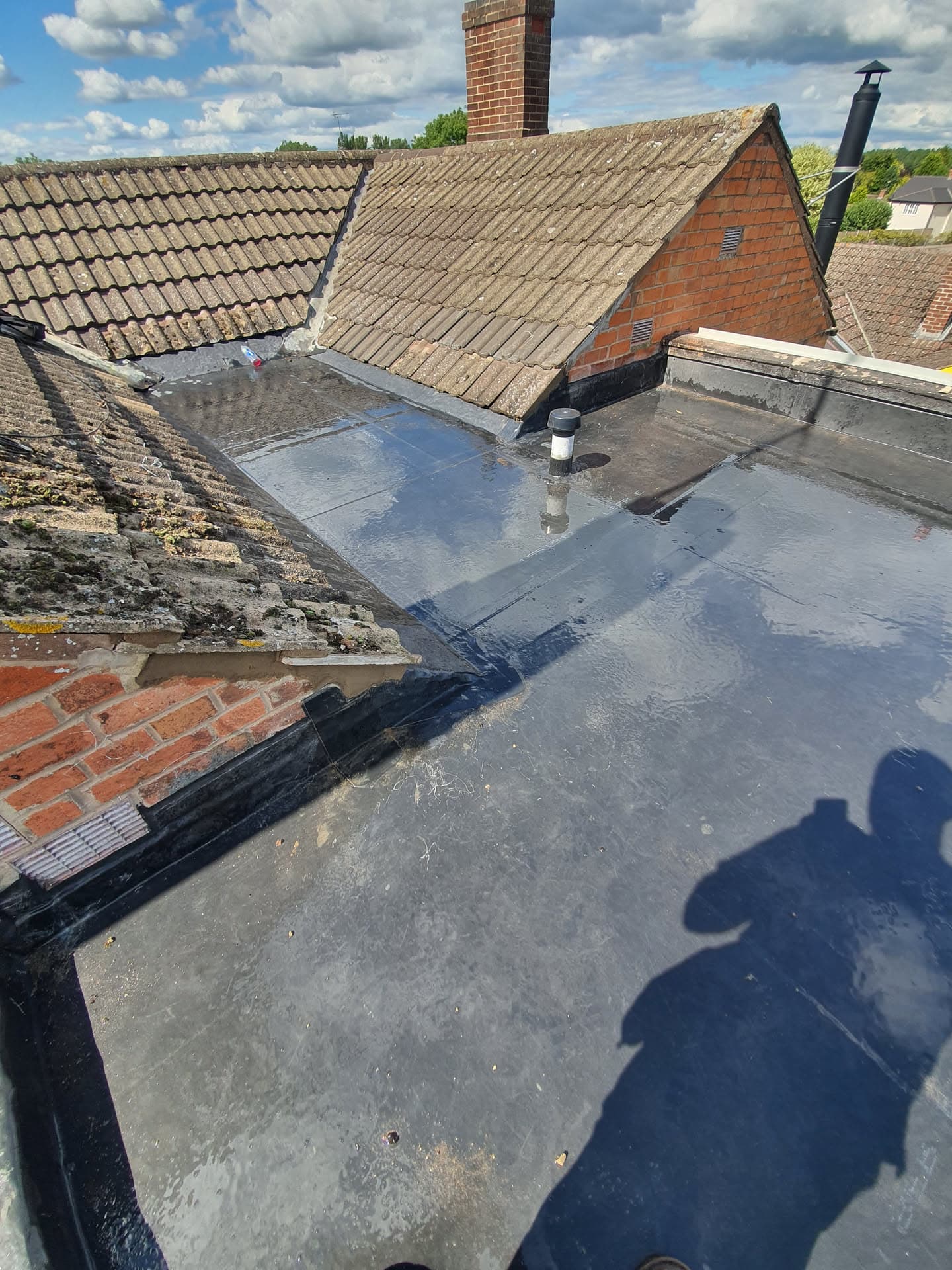 Flat roof with grey felt membrane meeting tiled pitched roof and brick chimney stack