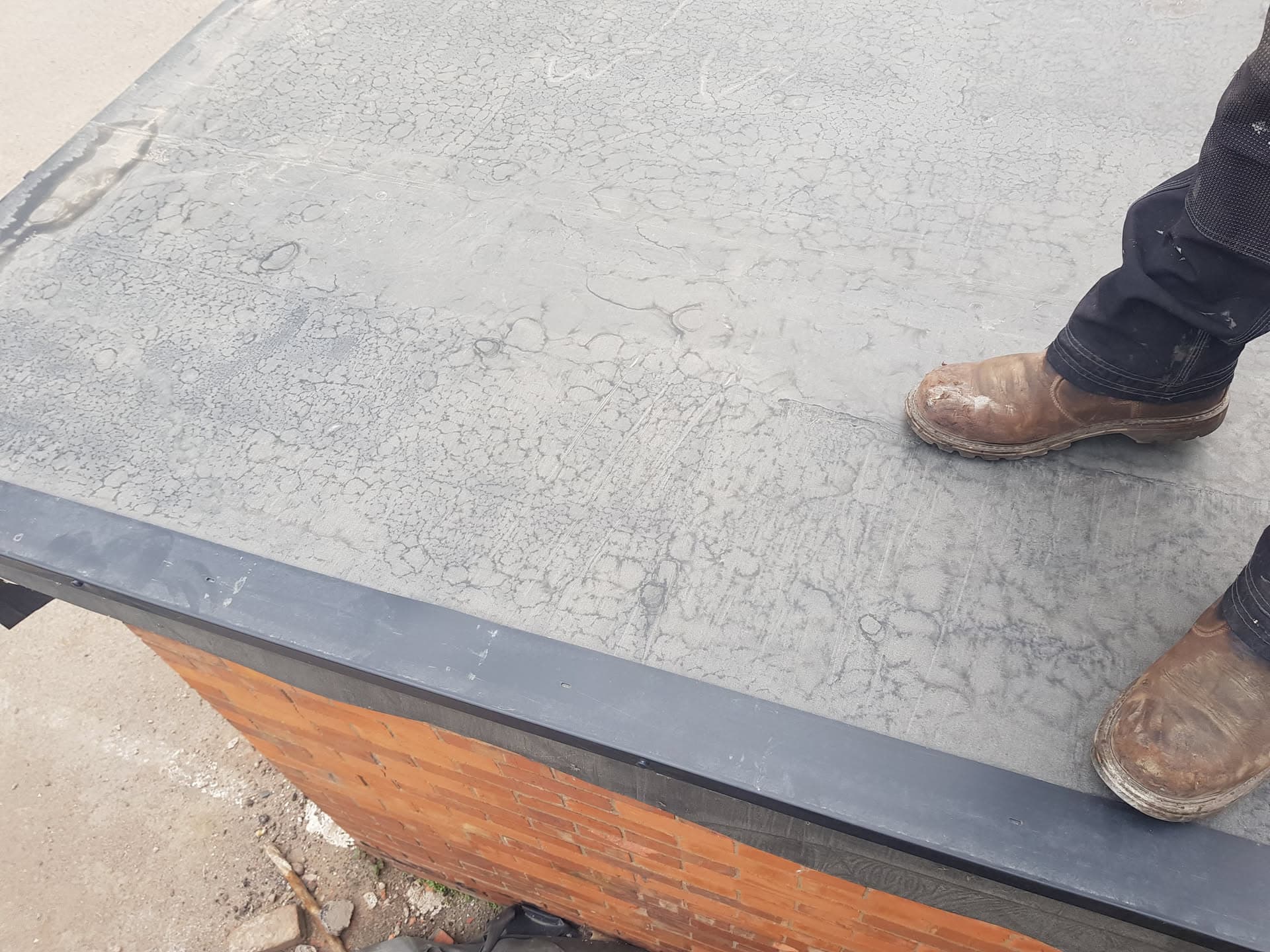 Fitter standing on grey GRP flat roof surface with fascia board visible below