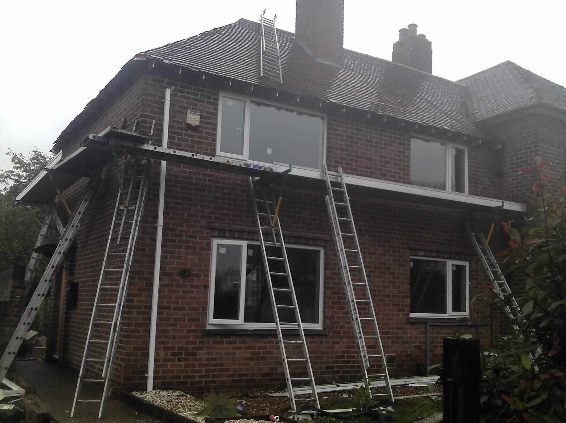 Pitched roof with dark grey tiles and chimney stack, ladders positioned for access