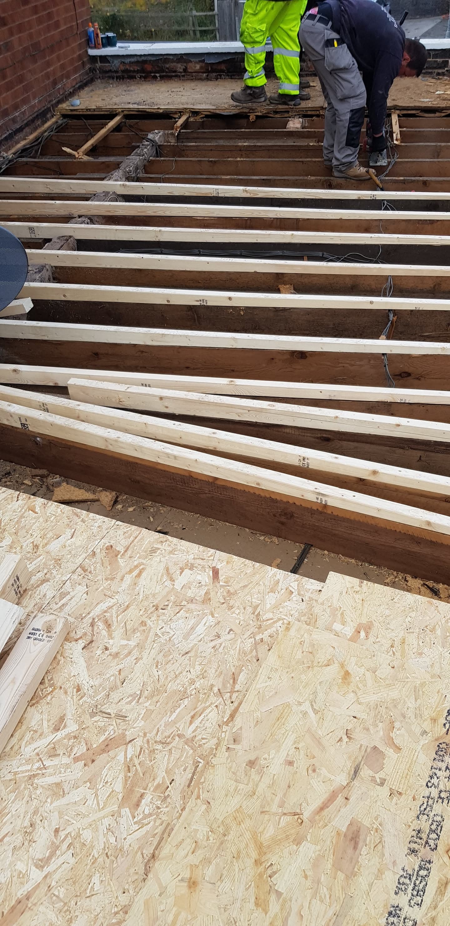Fitters installing timber joists for flat roof decking on residential extension