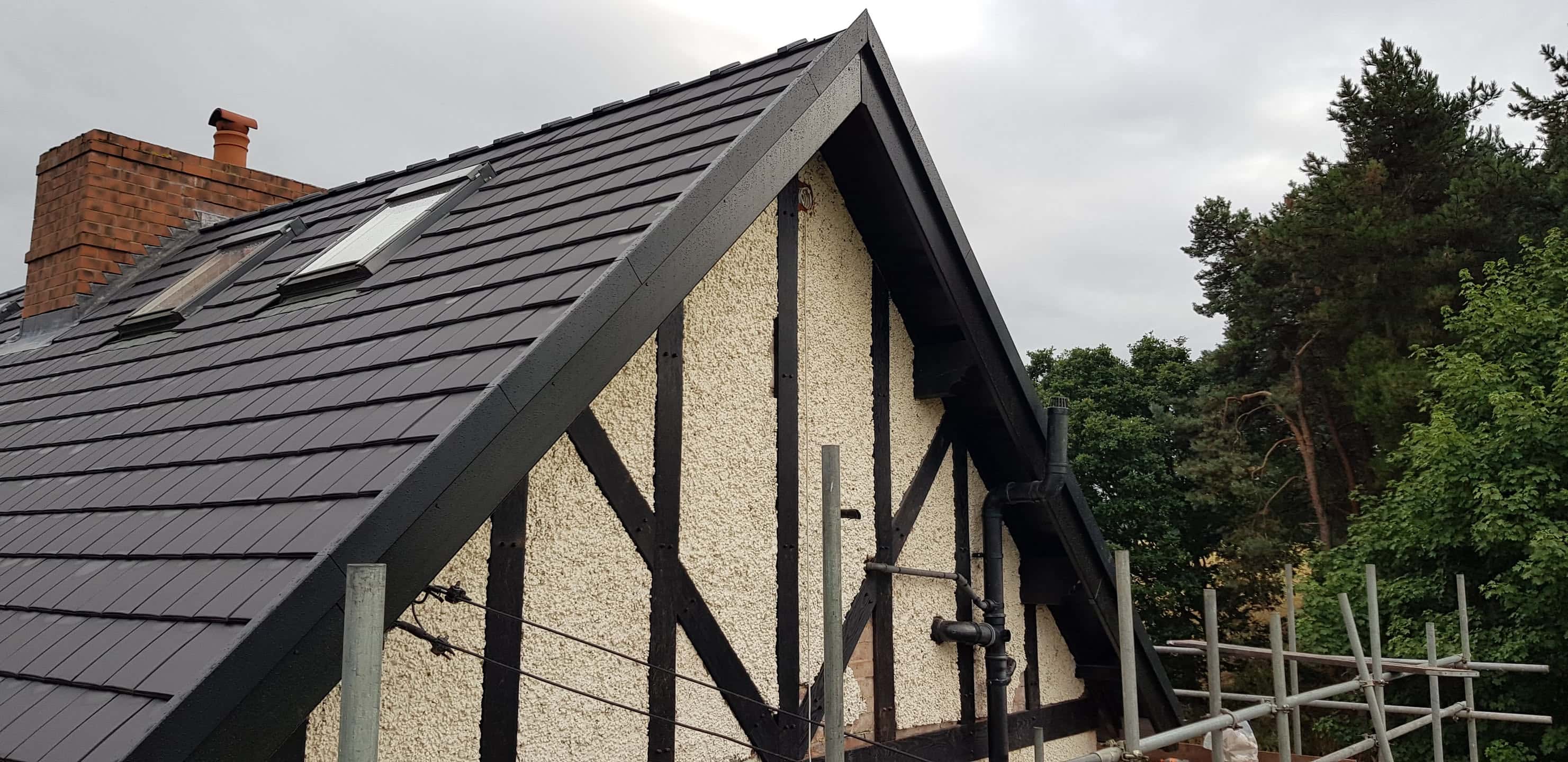 Newly installed grey slate pitched roof with dark fascias and bargeboards on gable end