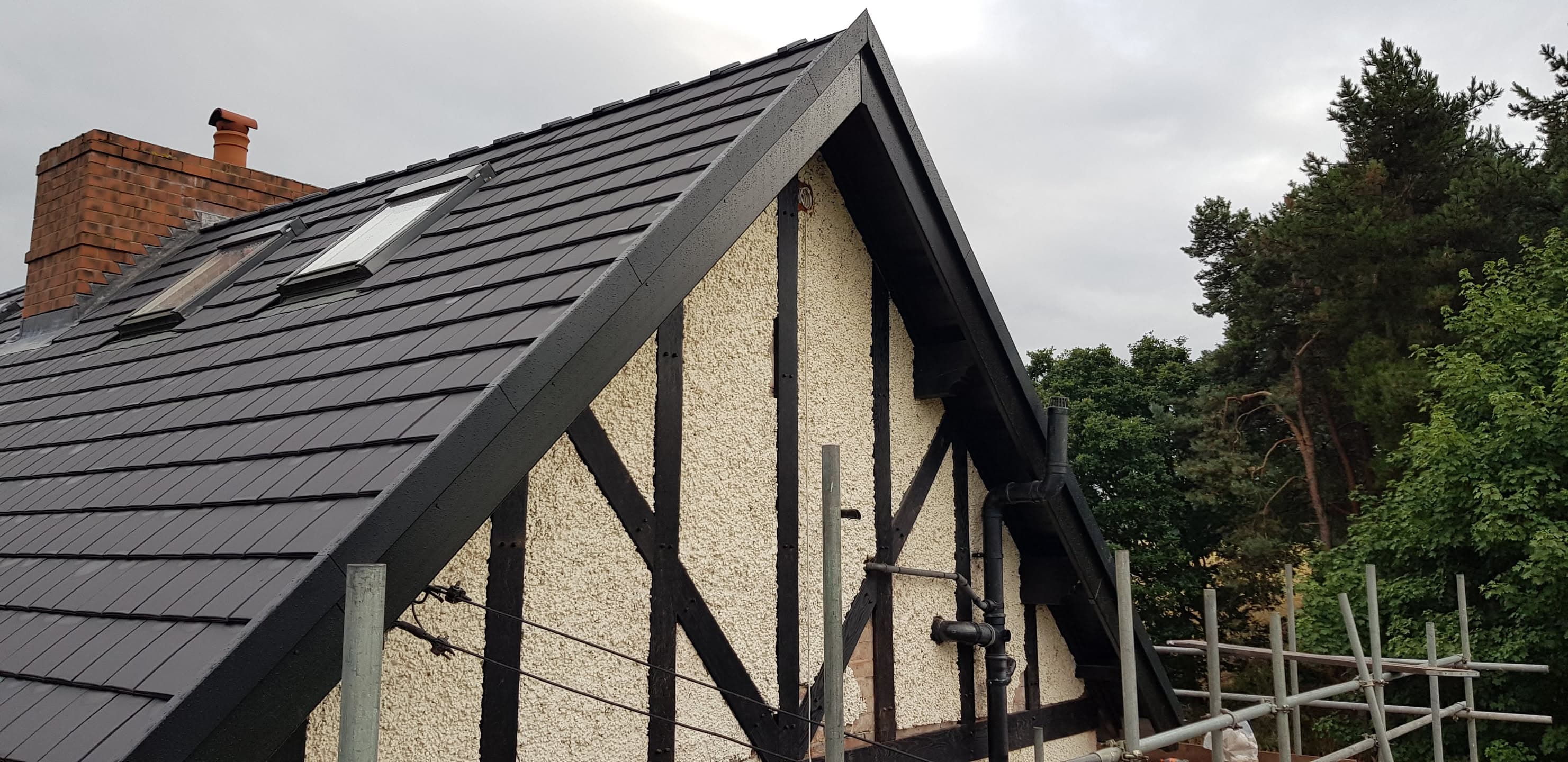 Newly installed grey slate pitched roof with dark fascias and bargeboards on gable end
