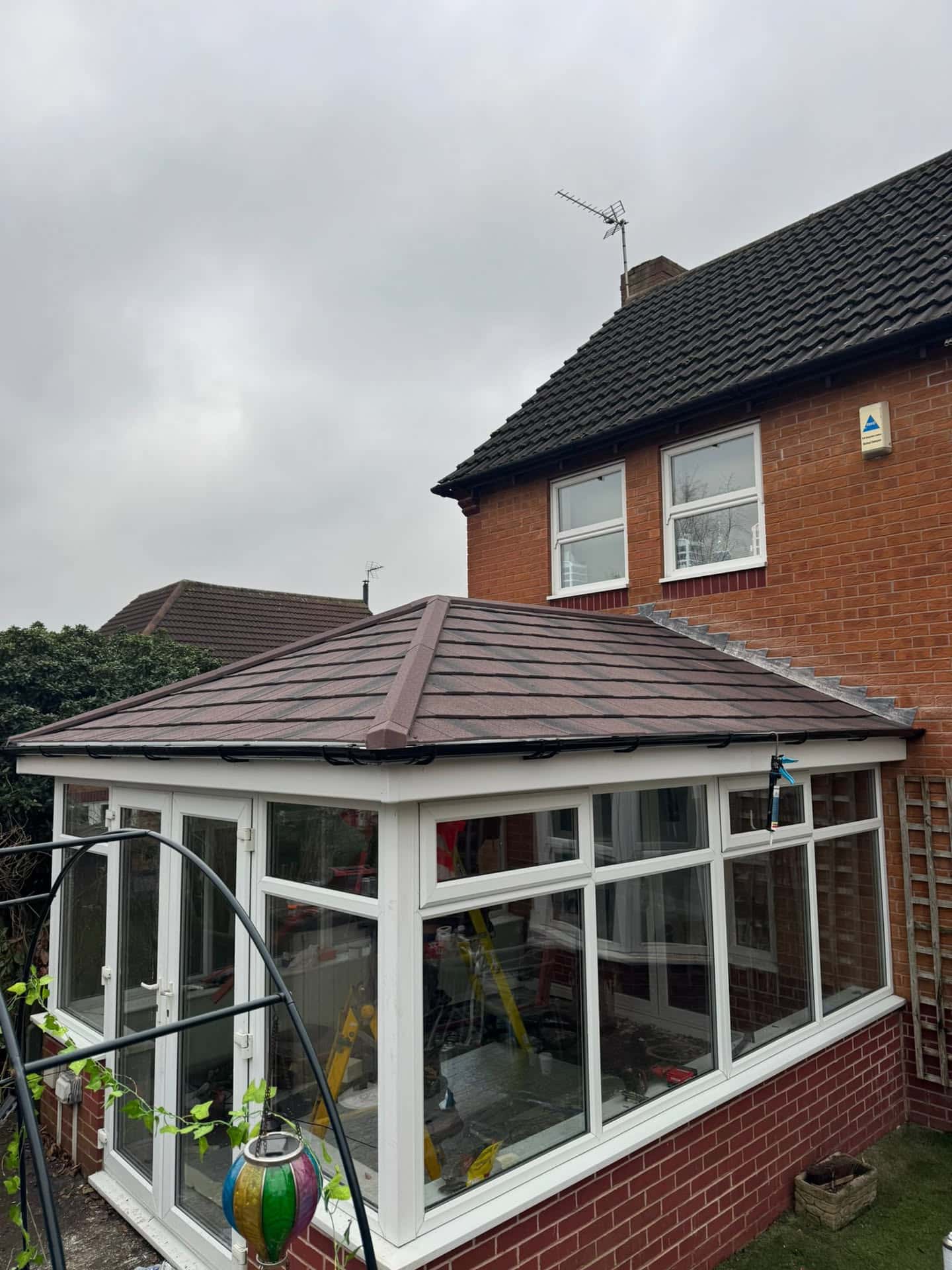Brown tiled conservatory roof with white uPVC frames on brick house