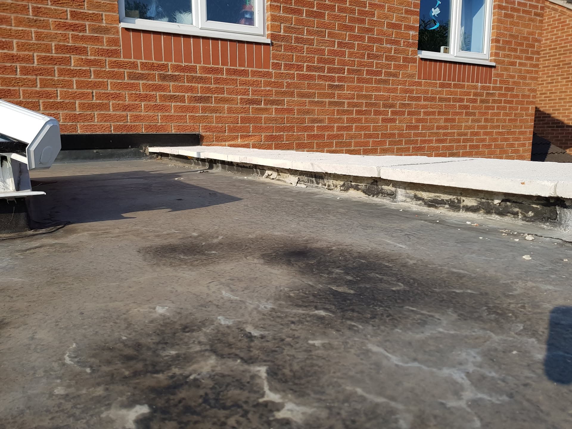 Flat roof with felt covering and concrete parapet edge on brick building
