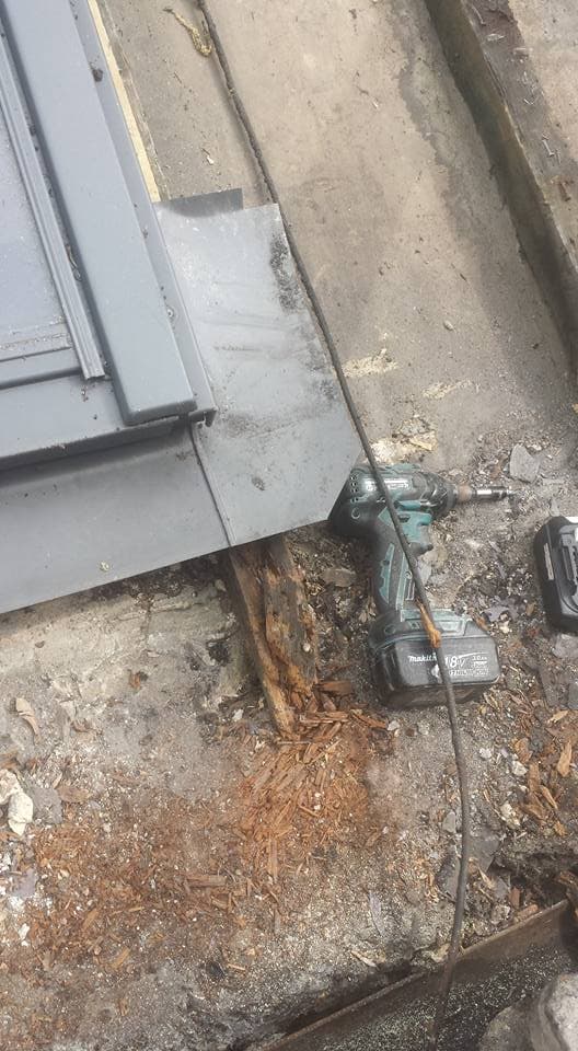 Flat roof repair work in progress with power drill and debris on grey felt surface
